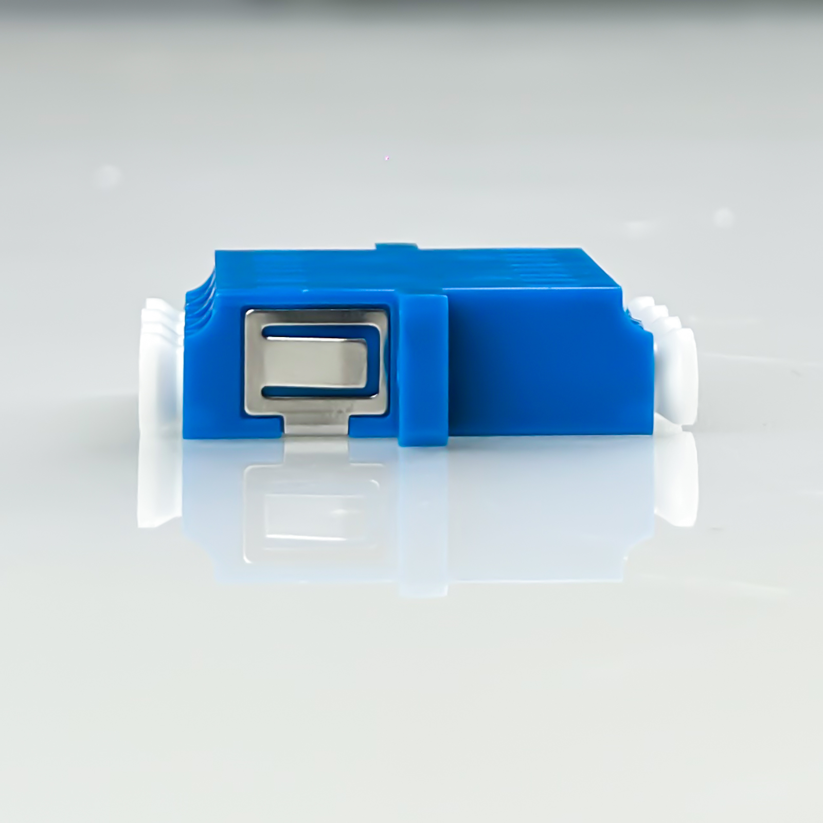 Ein blaues Adaptergehäuse mit einem silbernen Clip und weißen Endstücken auf reflektierendem Untergrund.