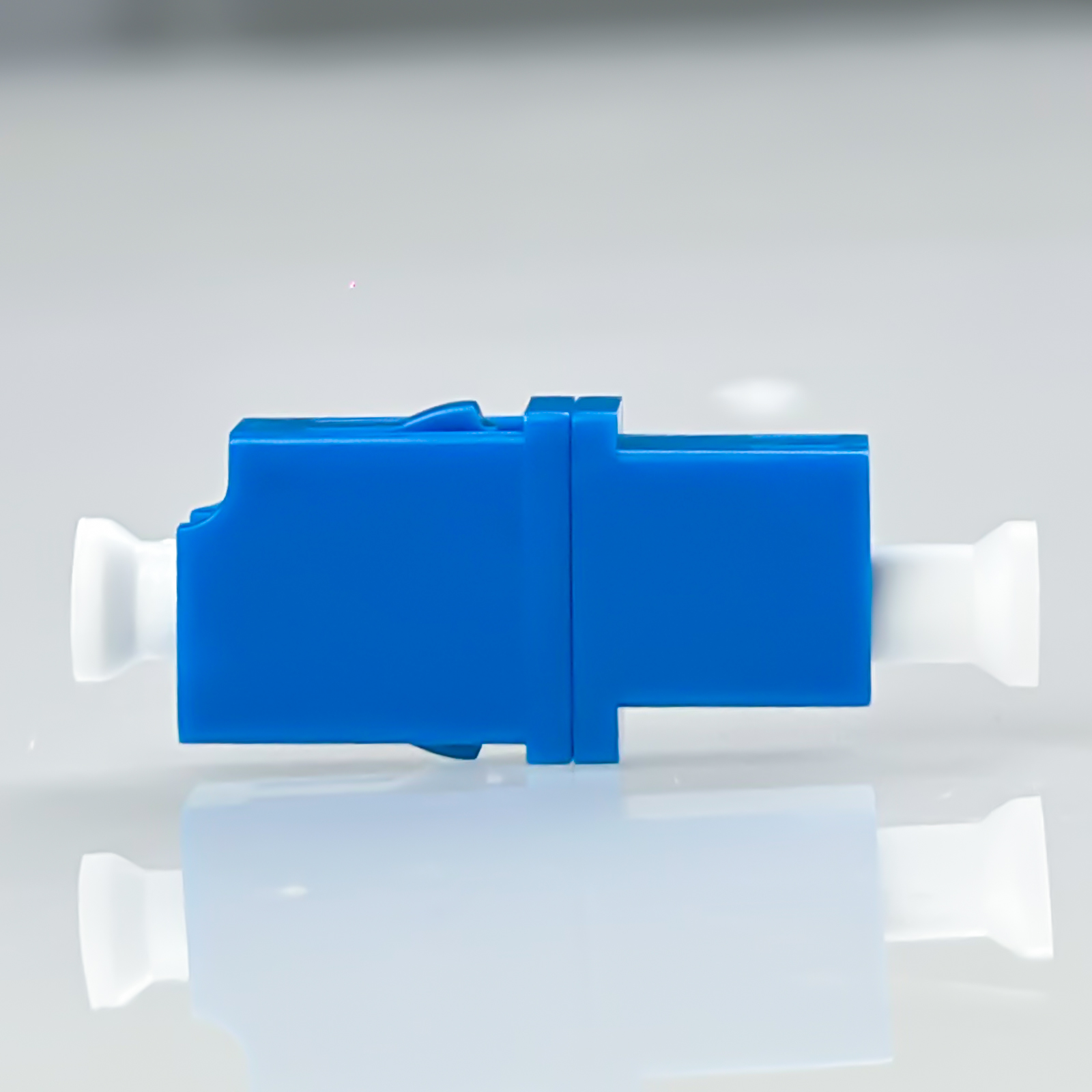 Ein blauer und weißer Glasfaseradapter liegt auf einer spiegelnden Fläche.