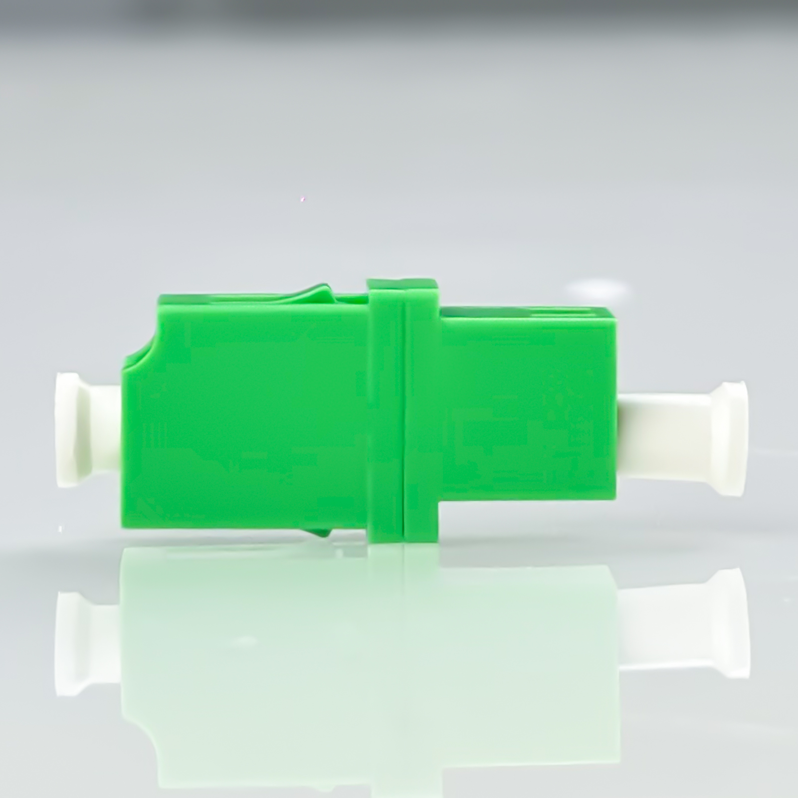 Grüner Fasersteckverbinder mit weißem Ende auf reflektierender Oberfläche.