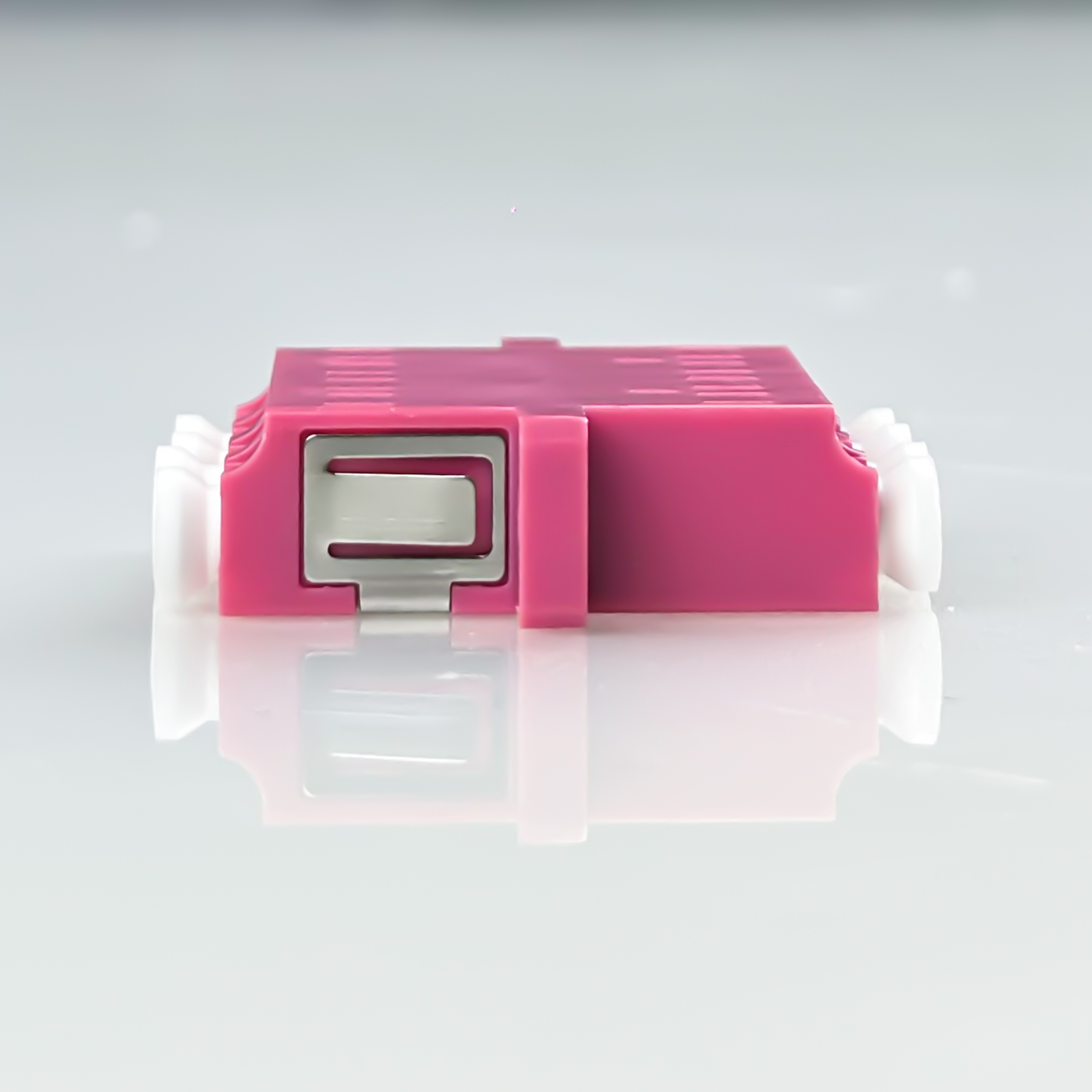 Ein pinker Stecker mit silbernem Clip und weißen Enden auf reflektierender Oberfläche.