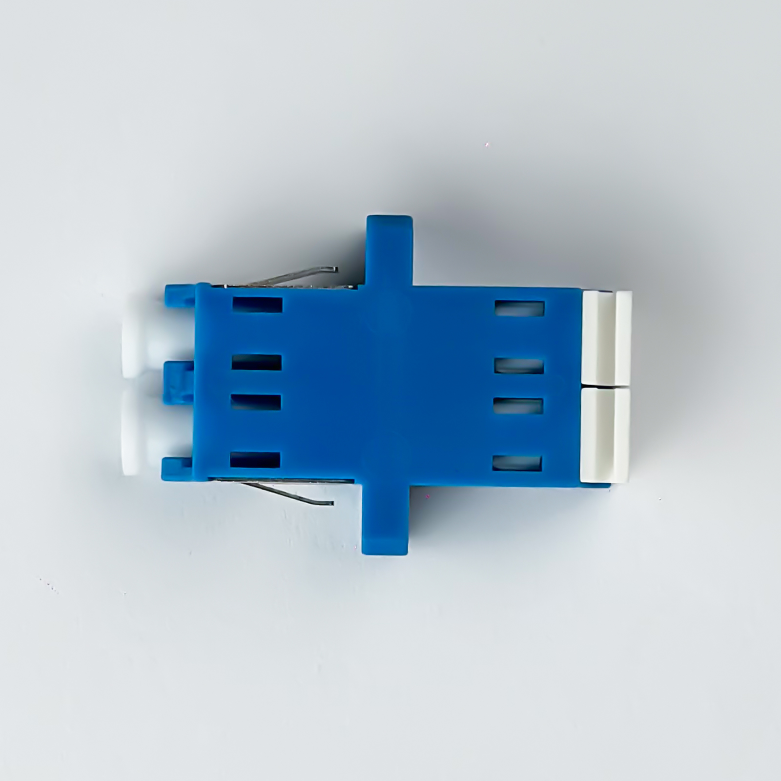 Ein blau-weißer Glasfaseradapter mit Metallclips auf weißem Hintergrund.