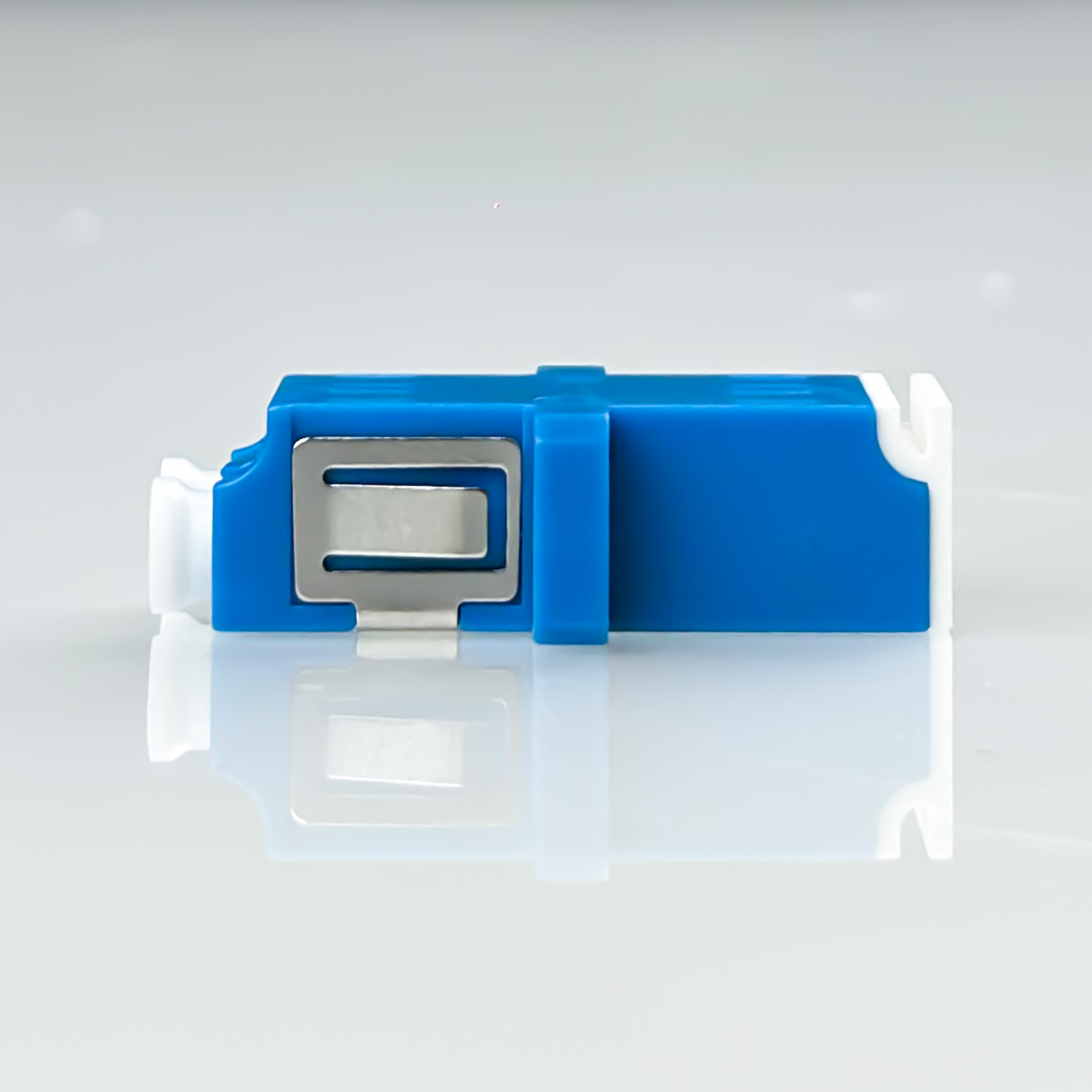 Ein blauer und weißer Glasfasersteckverbinder mit Metallclip auf glatter Oberfläche.