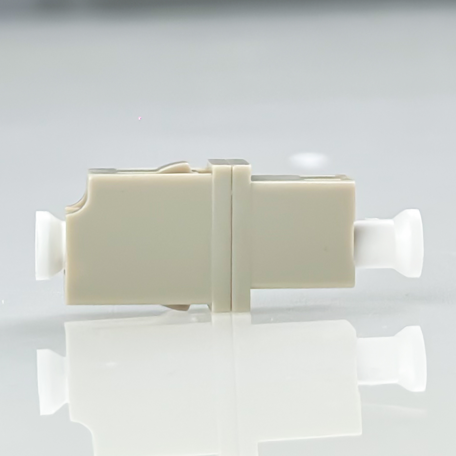 Ein cremefarbener Stecker mit weißen Enden auf einem spiegelnden weißen Hintergrund.