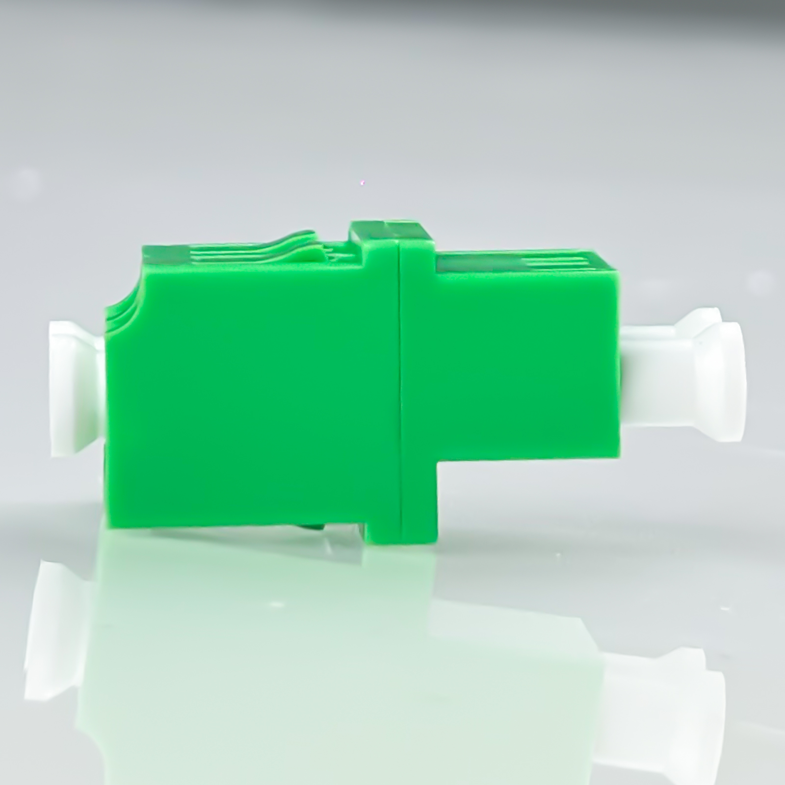 Ein grüner und weißer optischer Stecker auf reflektierender Oberfläche.