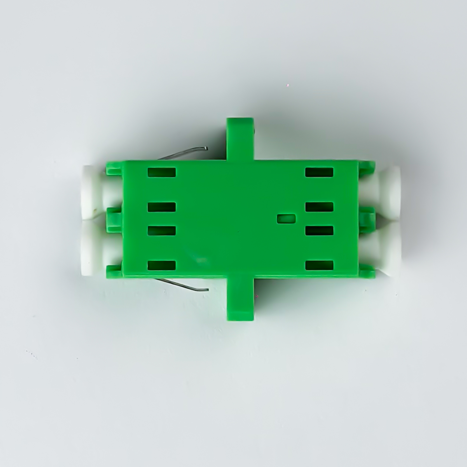 Grüner Plastikadapter mit weißen Endstücken und Metallclips, auf weißem Hintergrund.