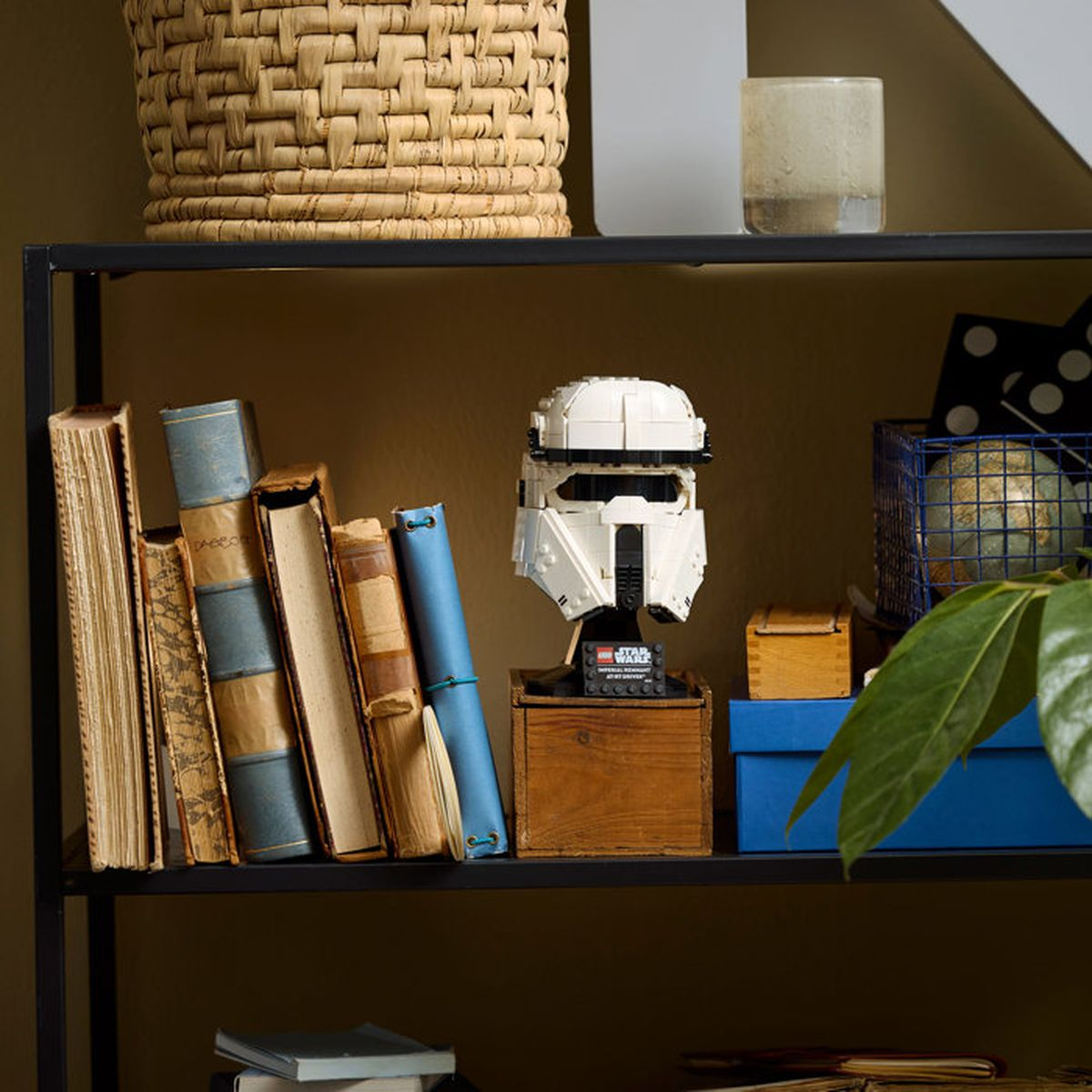Un casco da stormtrooper Lego si trova su un piedistallo di legno accanto a libri e un globo.