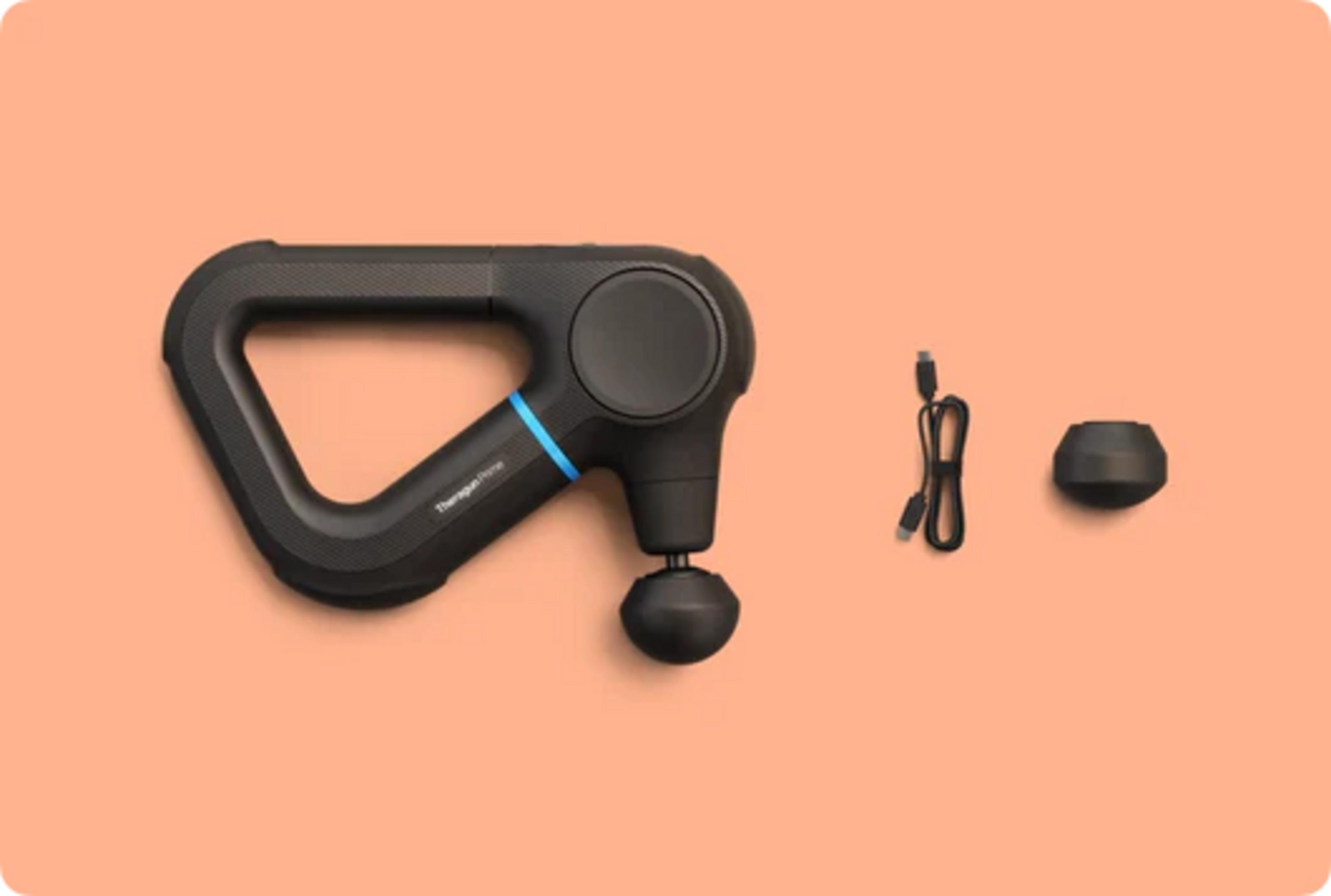 Pistola de masaje negra con cable de carga y accesorio sobre fondo coral.