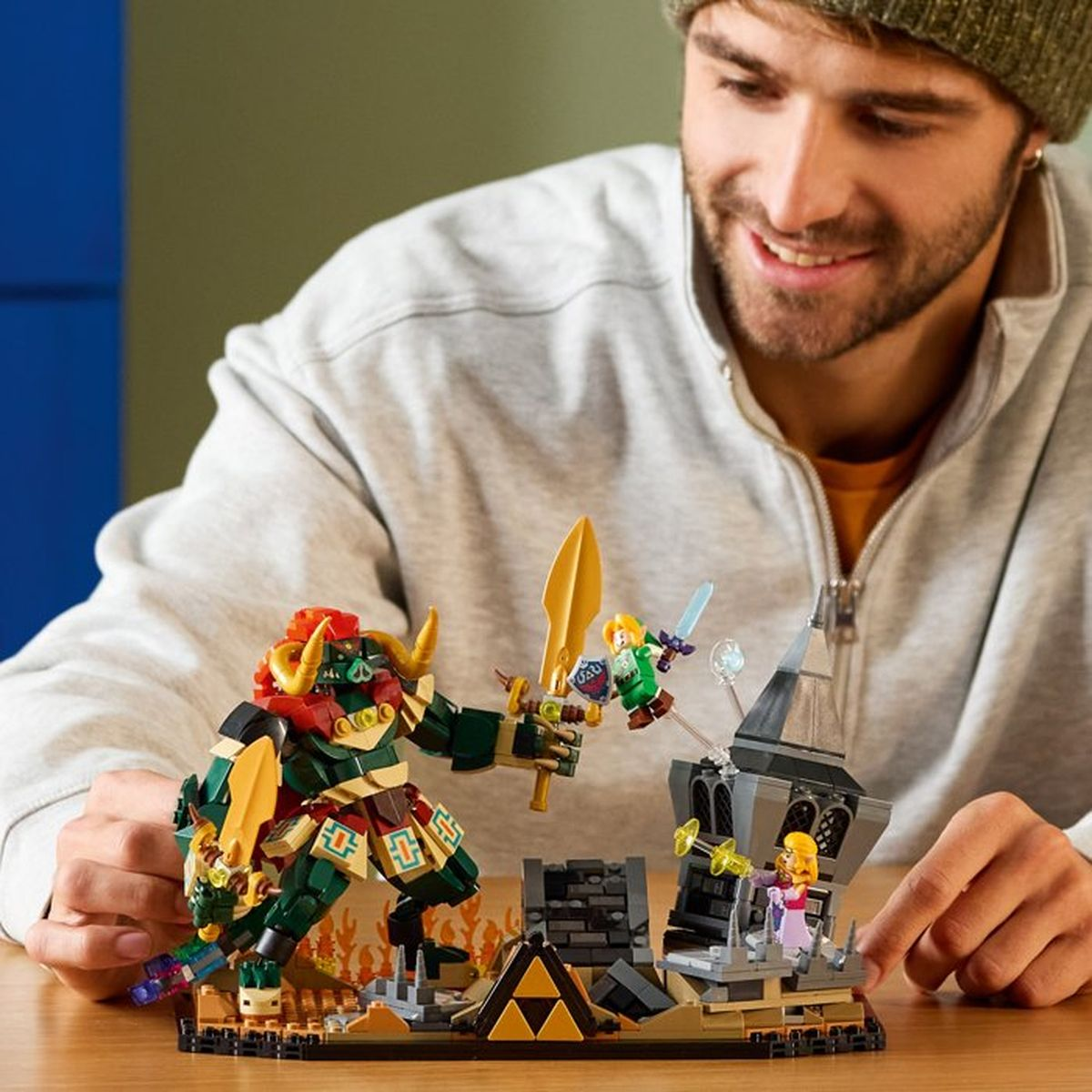 Uomo gioca con figure Lego: Ganondorf, Link e Zelda davanti a un castello.