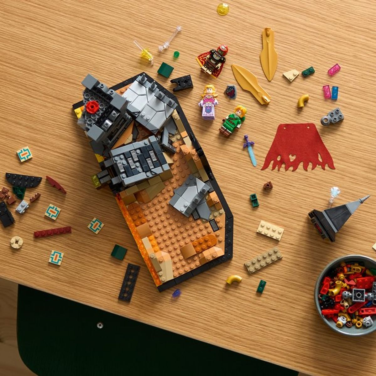 Giocattoli Lego su un tavolo di legno, tra cui un castello, figure e mantelli rossi.