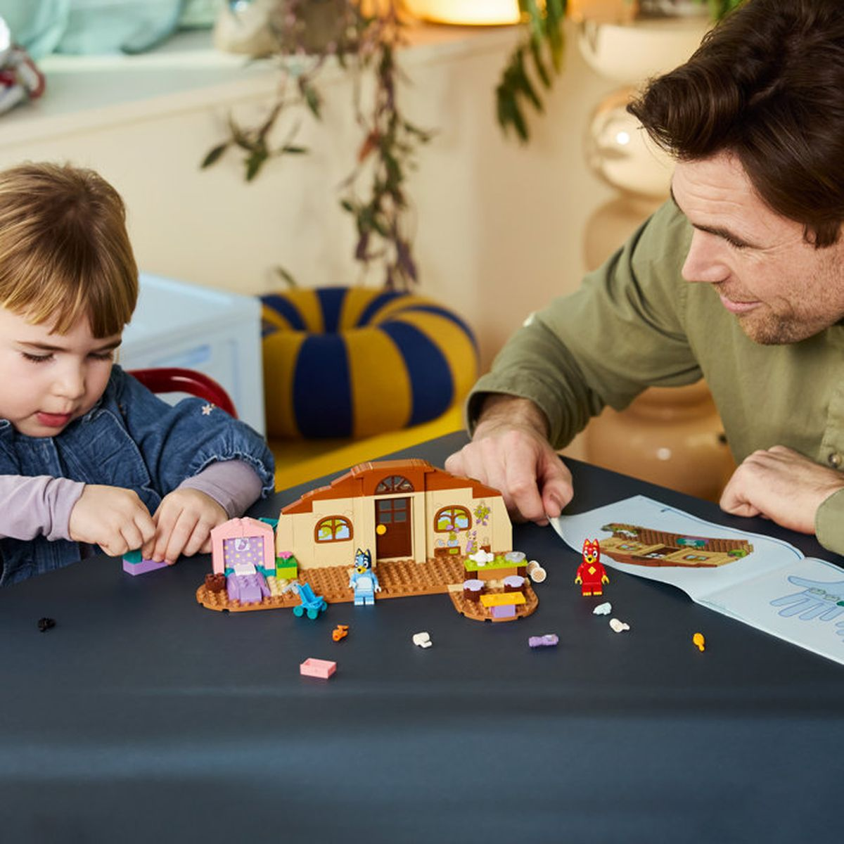 Un uomo e un bambino costruiscono una casa Lego con figure e istruzioni.