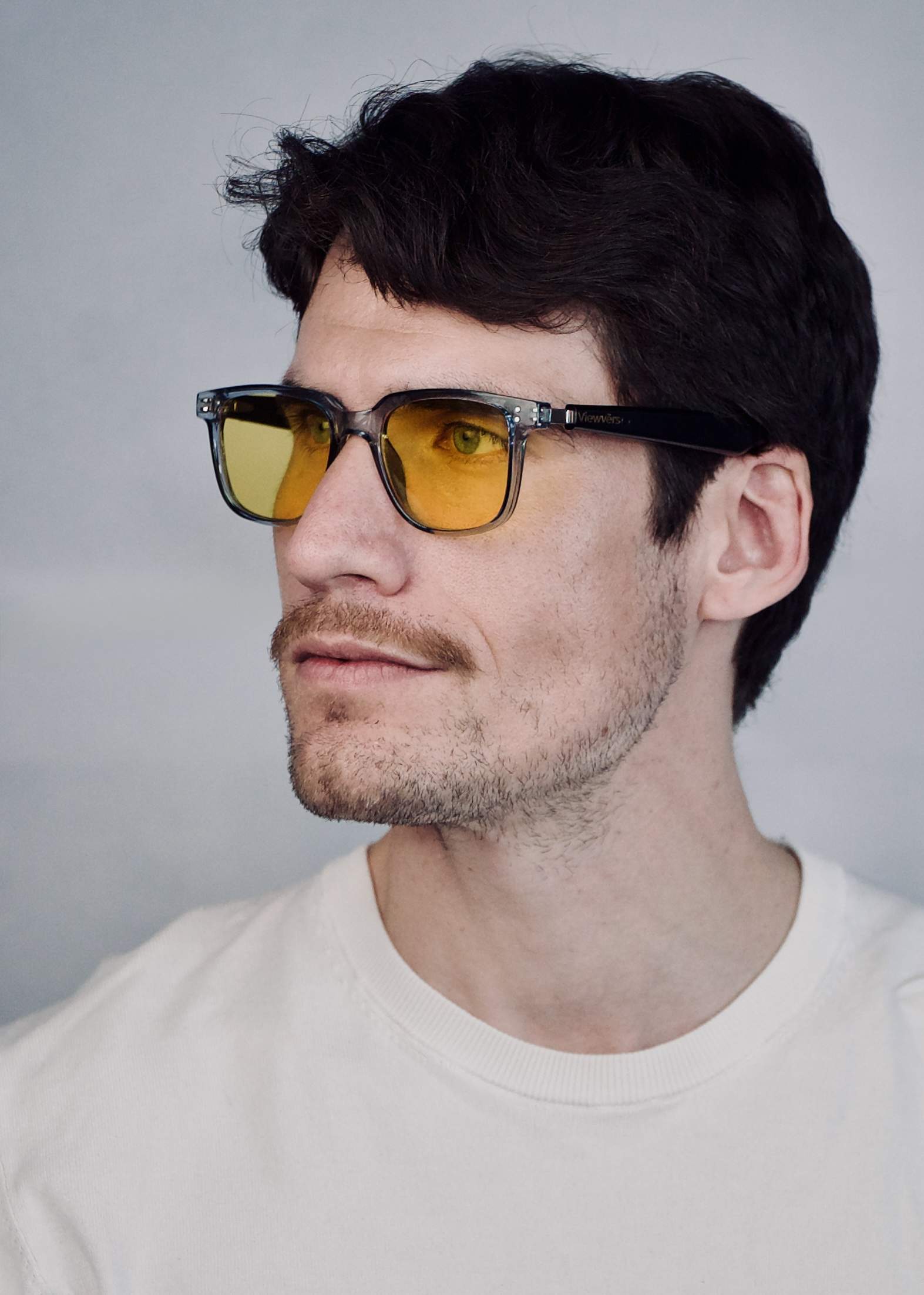 Hombre de pelo oscuro viste camiseta blanca y gafas amarillas.