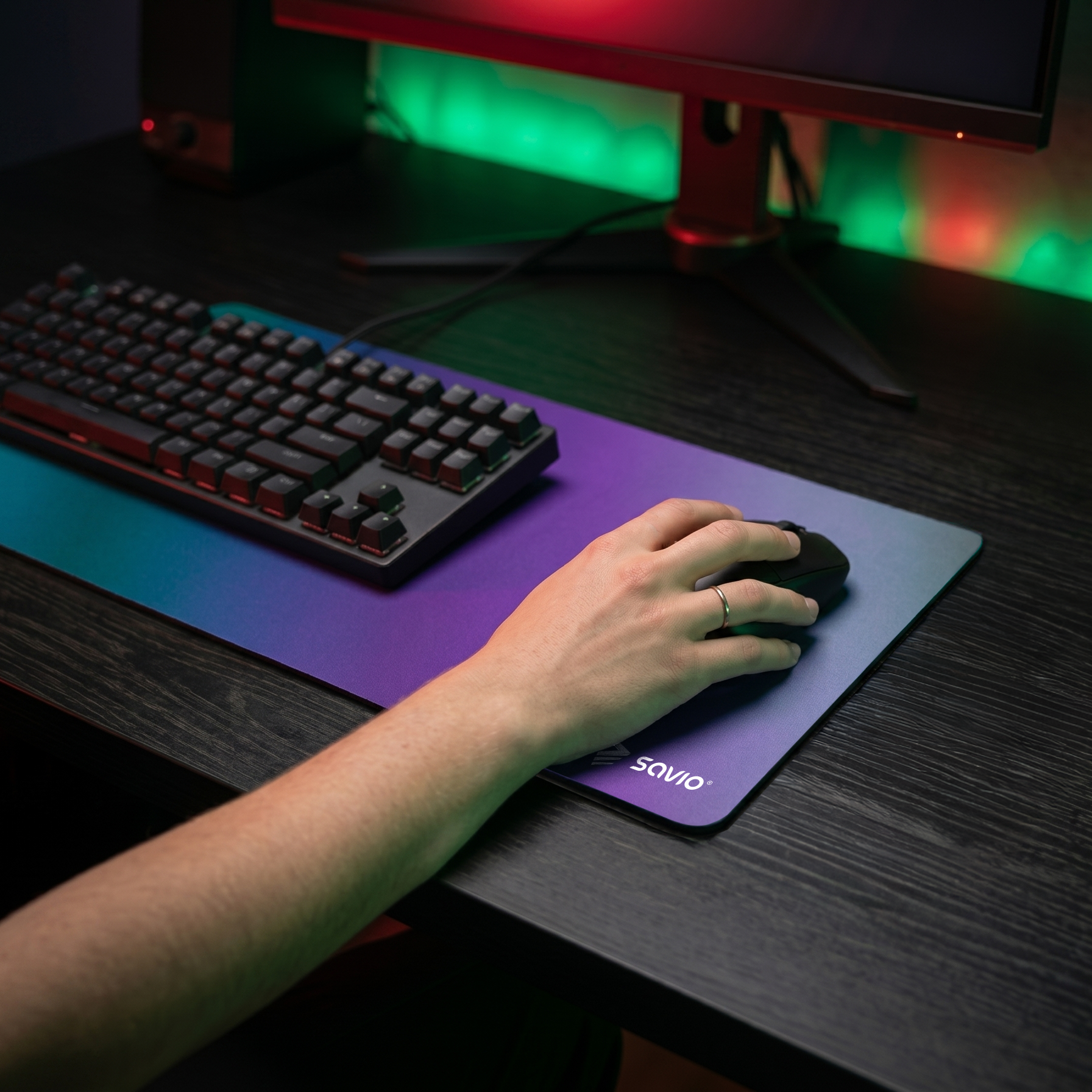 Dłoń używa myszy na biurku z klawiaturą i podświetlonym monitorem.