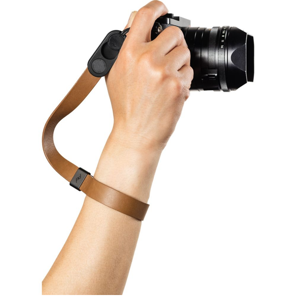 Een hand houdt een camera vast met een bruine lederen polsband.