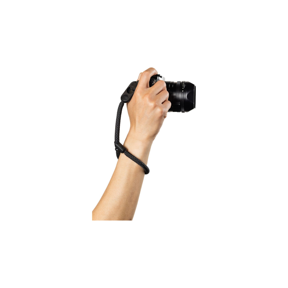 Een hand houdt een zwarte camera met een zwarte riem vast.