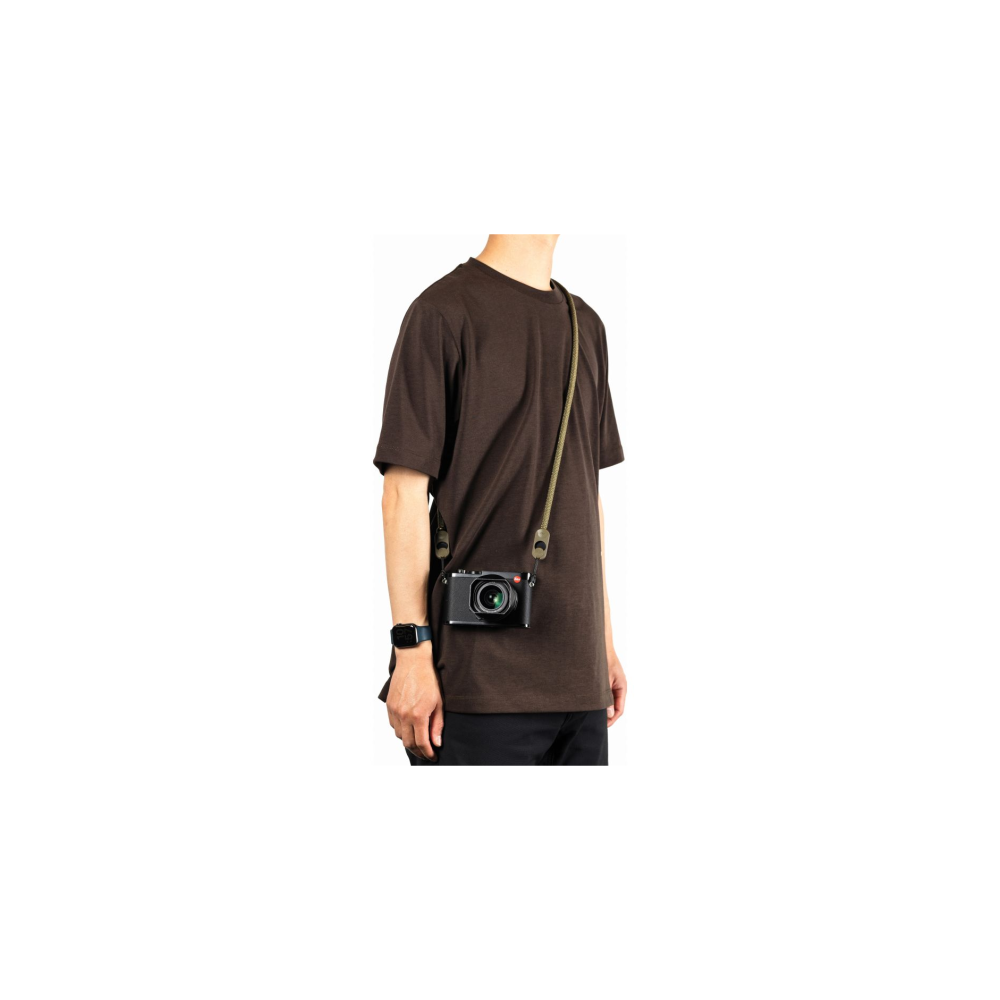 Person in brown t-shirt with camera and olive green strap over shoulder.
