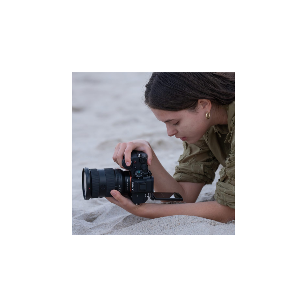 Een vrouw in een groen jack ligt op zand en houdt een zwarte Sony-camera vast.