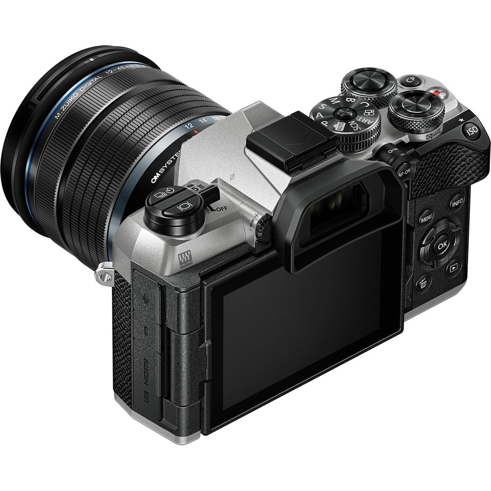 Zilveren OM System camera met zwarte M.Zuiko lens, schuin van voren. Met klapscherm.
