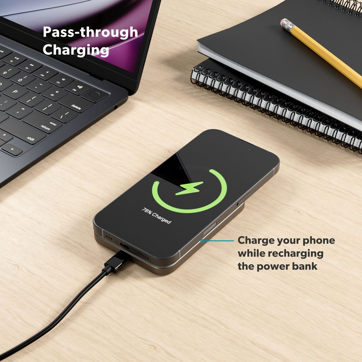 Uno smartphone si carica via cavo, accanto a un laptop e quaderni.