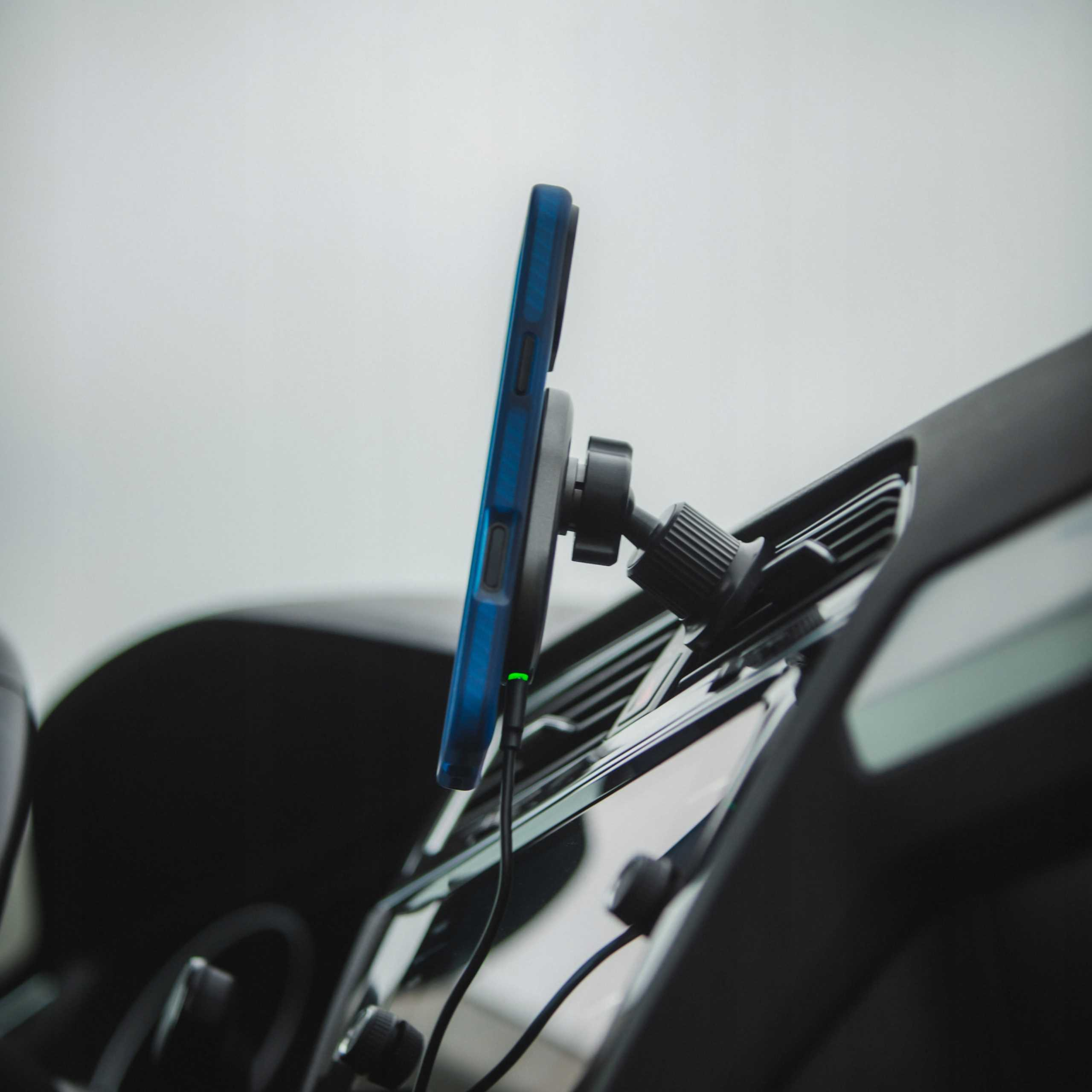 Niebieski smartfon w uchwycie samochodowym, ładuje się zielonym światłem.