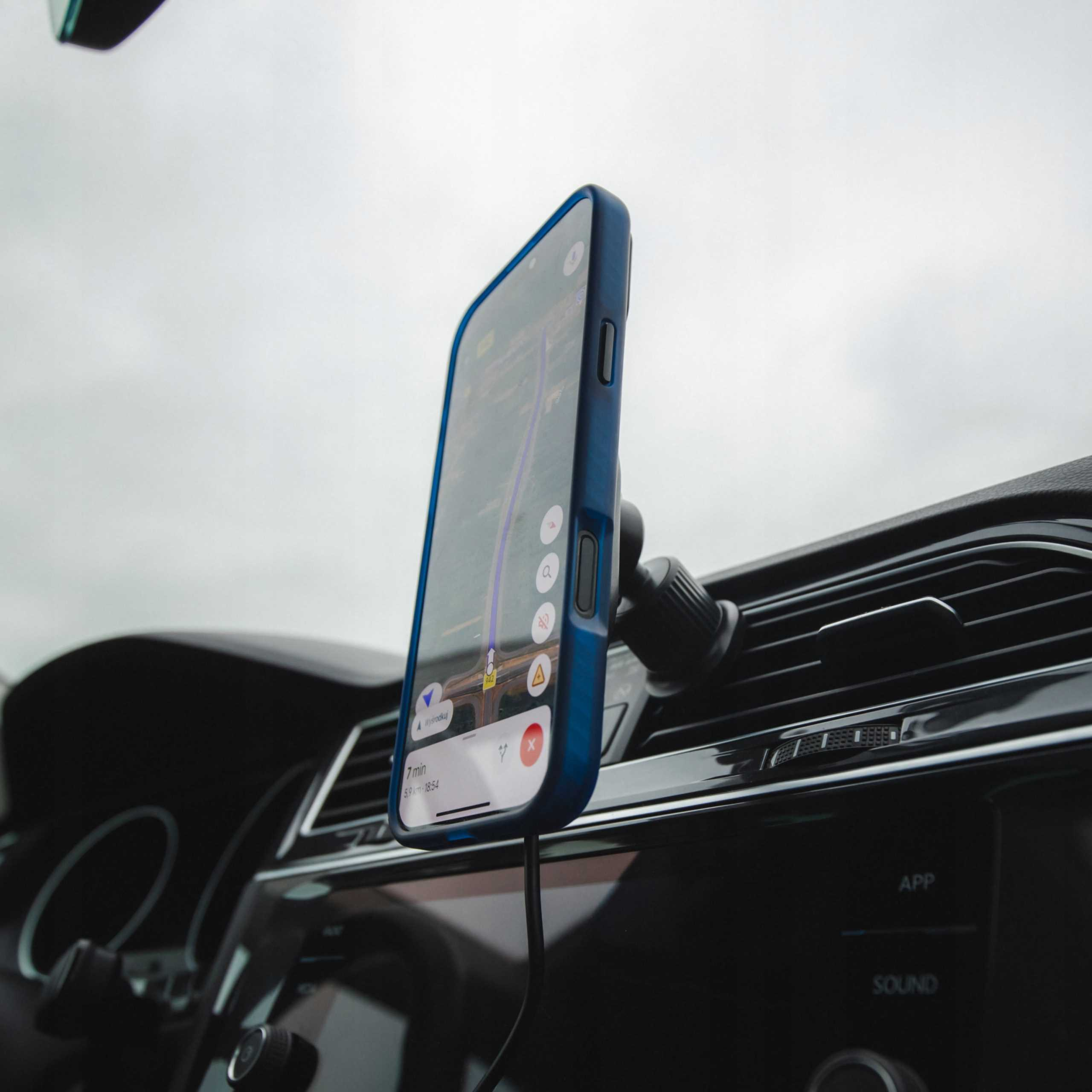 Smartfon z aplikacją nawigacyjną zamontowany na kratce wentylacyjnej samochodu.