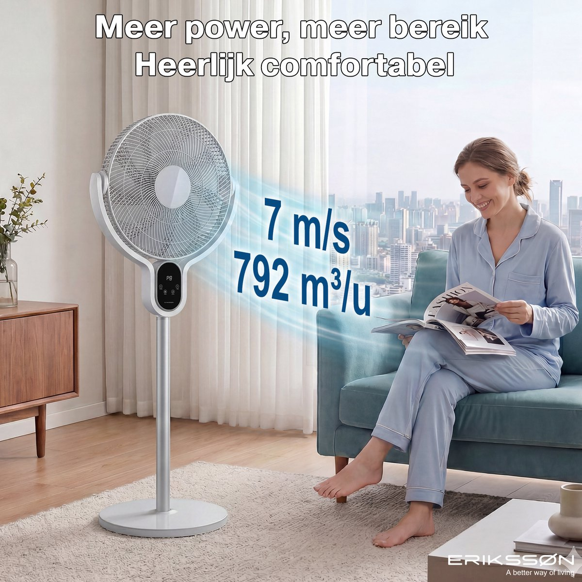 Un ventilador blanco de pie con pantalla digital está junto a un sofá donde una mujer lee.