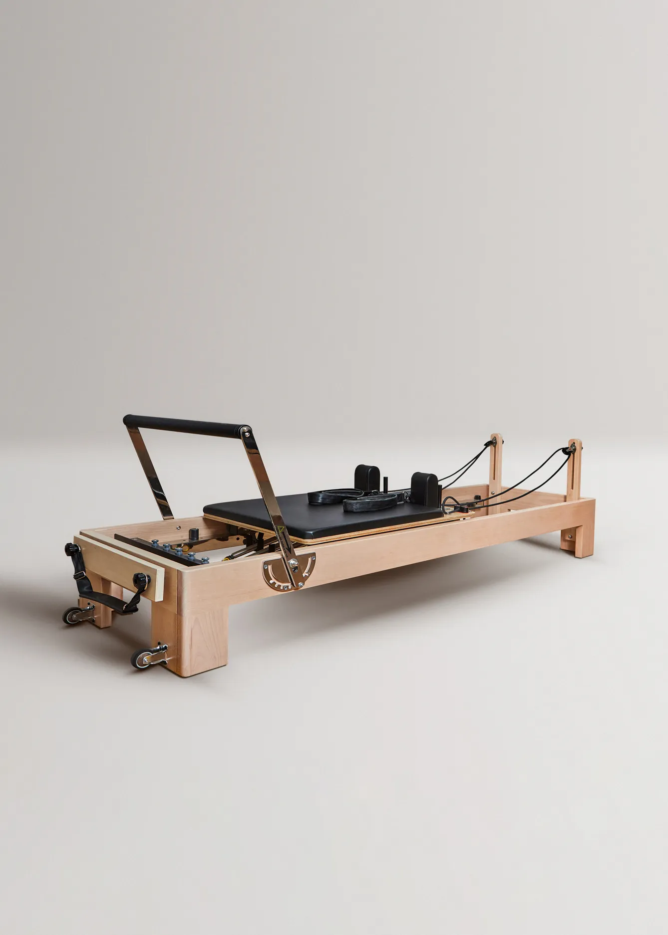 Un reformer de pilates de madera con carro acolchado negro y cuerdas.