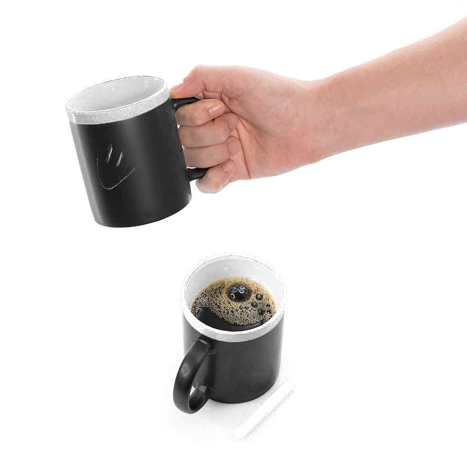 Mano che tiene tazza nera con smiley, accanto tazza piena di caffè.