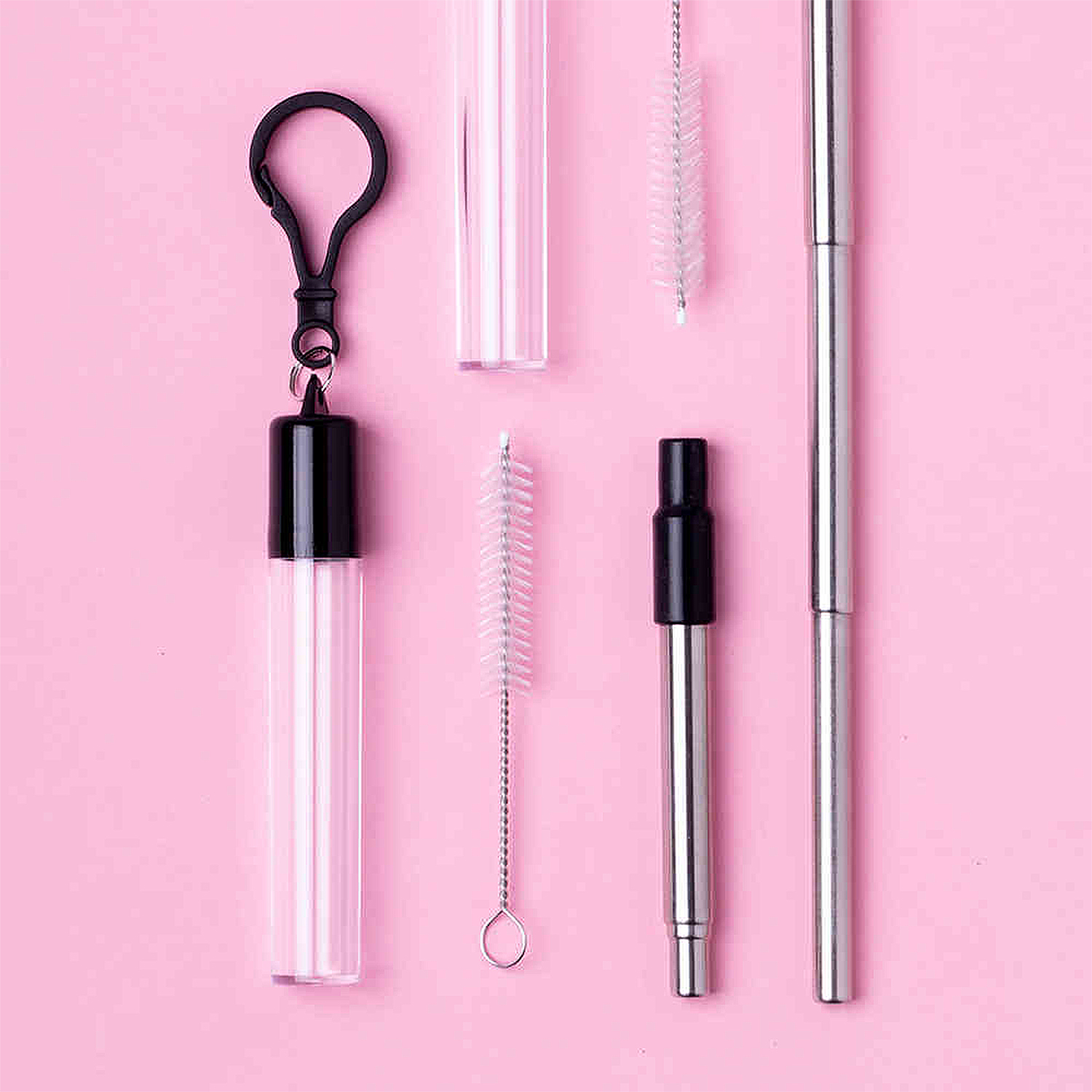 Cannucce riutilizzabili con spazzolini e custodia su sfondo rosa.