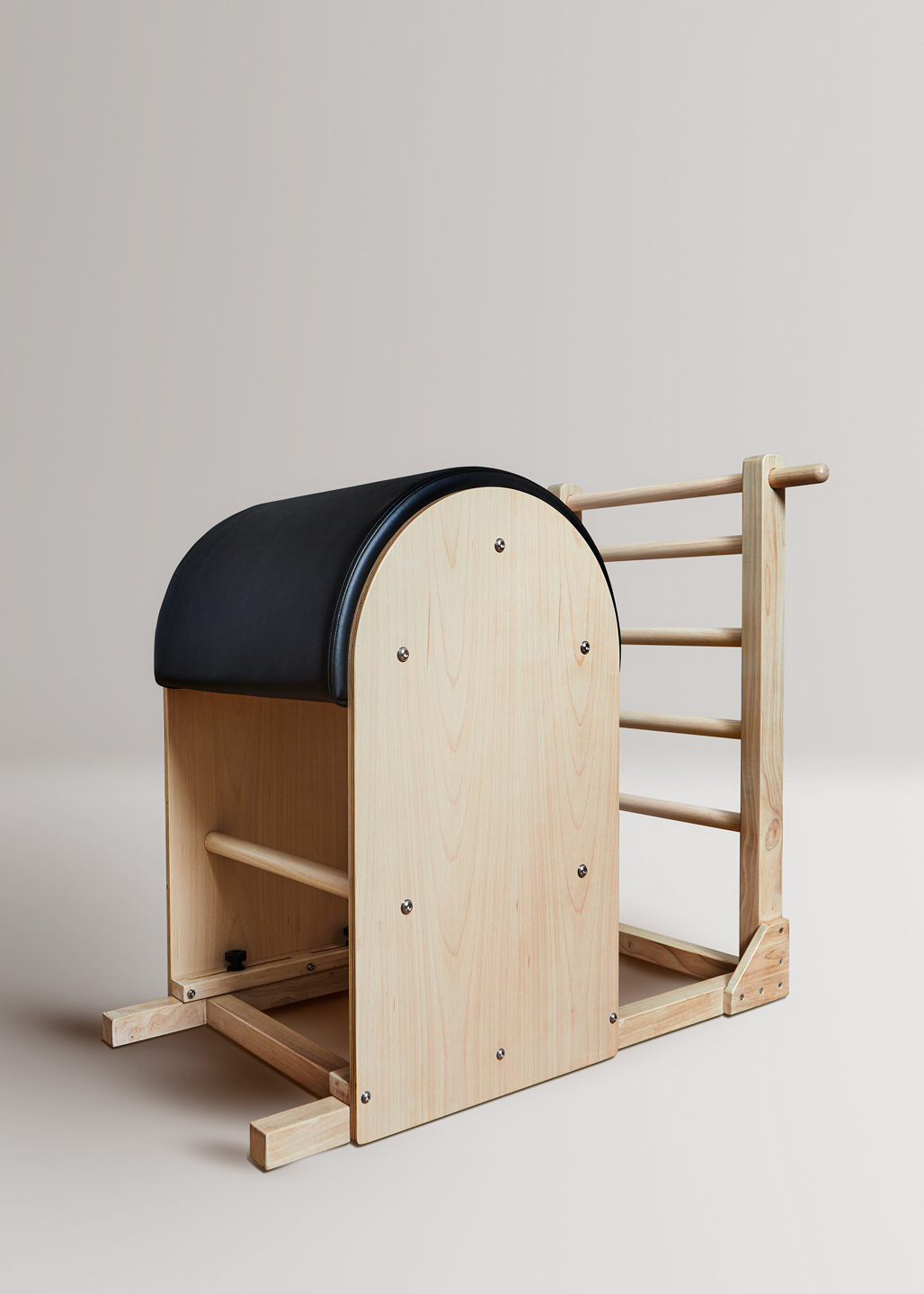 Un barril de Pilates de madera con acolchado negro y una escalera.