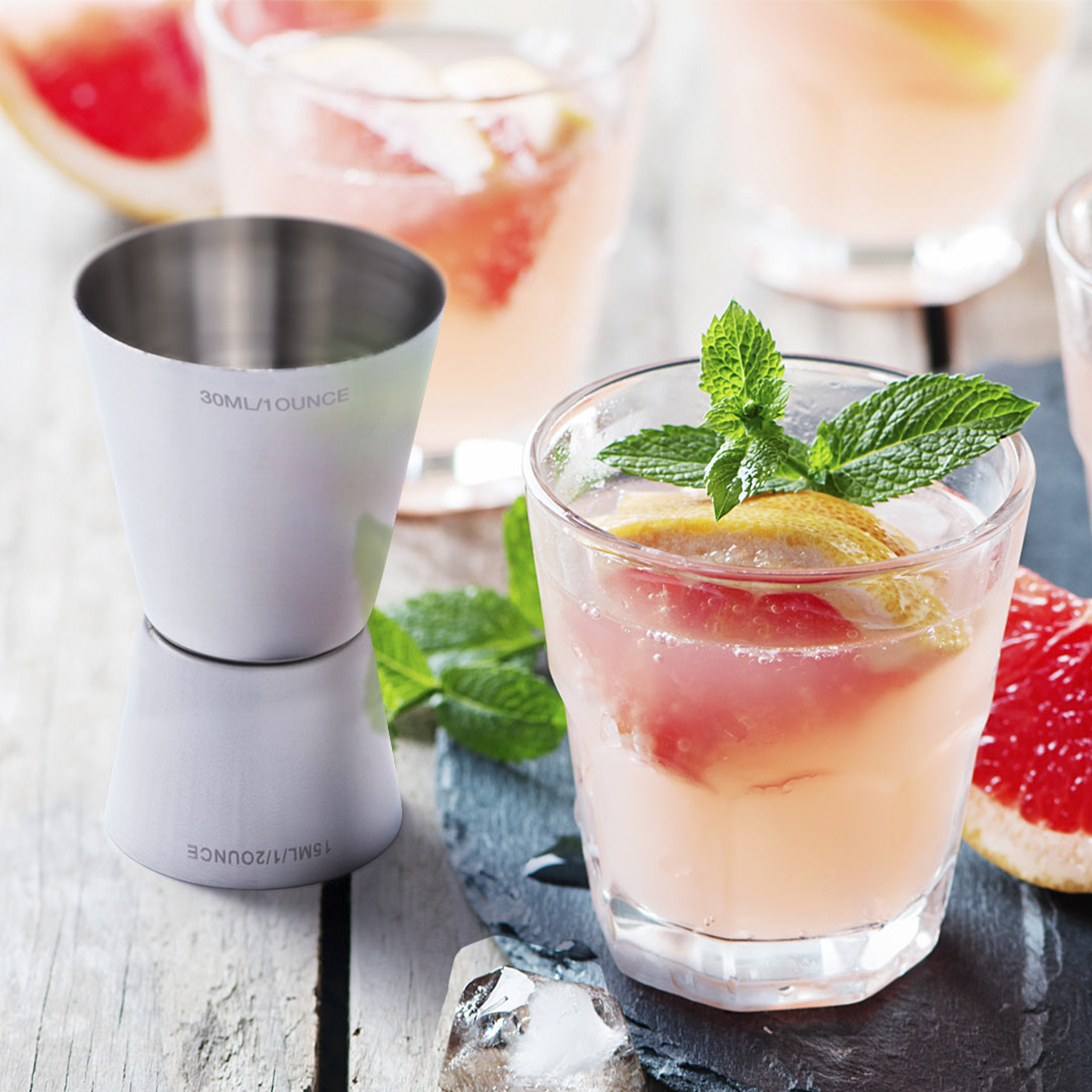 Un jigger e drink al pompelmo rosa con menta e ghiaccio su tavolo di legno.
