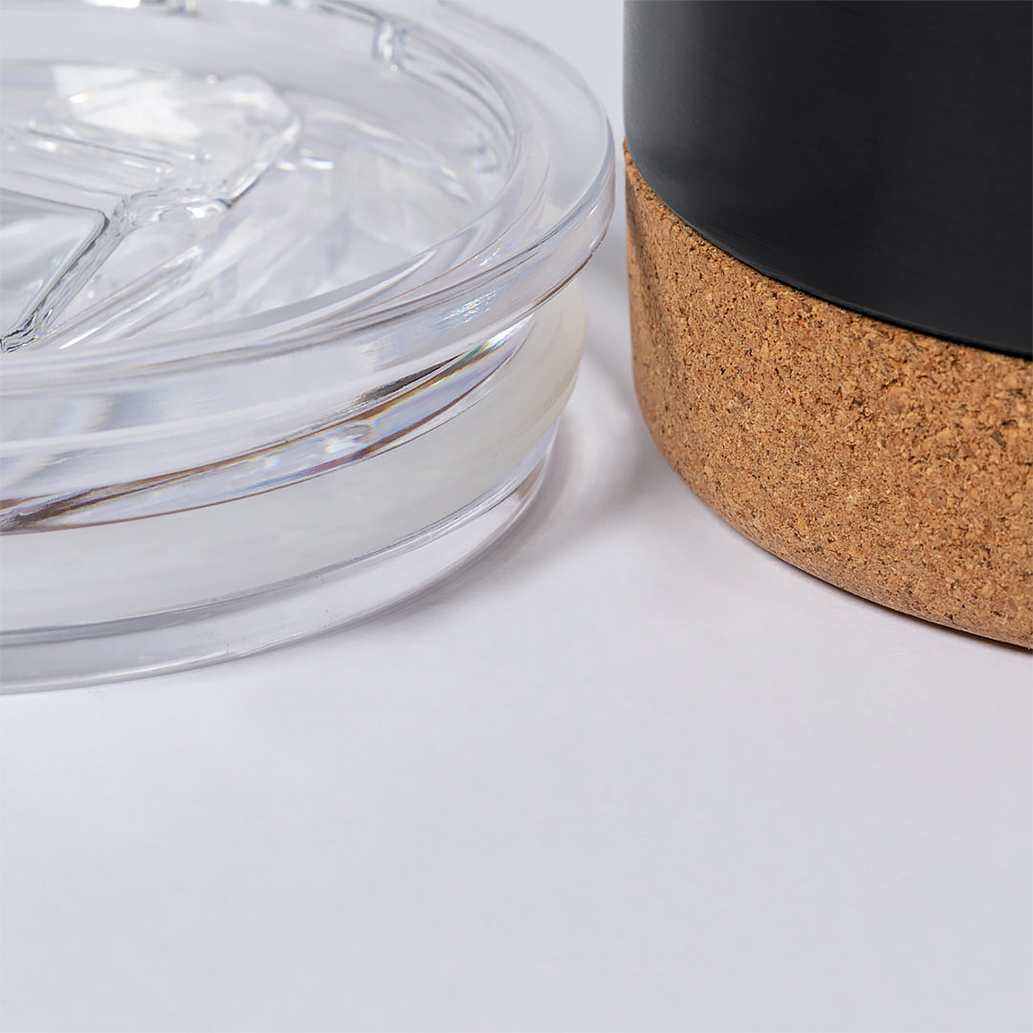 Primer plano de una tapa transparente y una taza negra con base de corcho.
