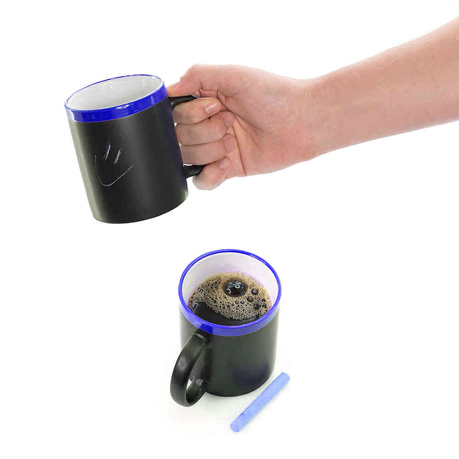 Mano che tiene tazza nera con faccina, accanto tazza piena di caffè e gesso.