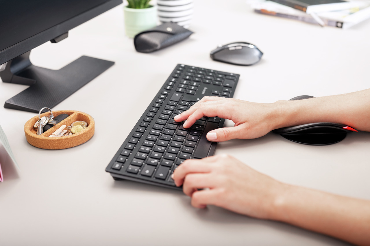 Mani che digitano su una tastiera nera con mouse e chiavi su una scrivania.