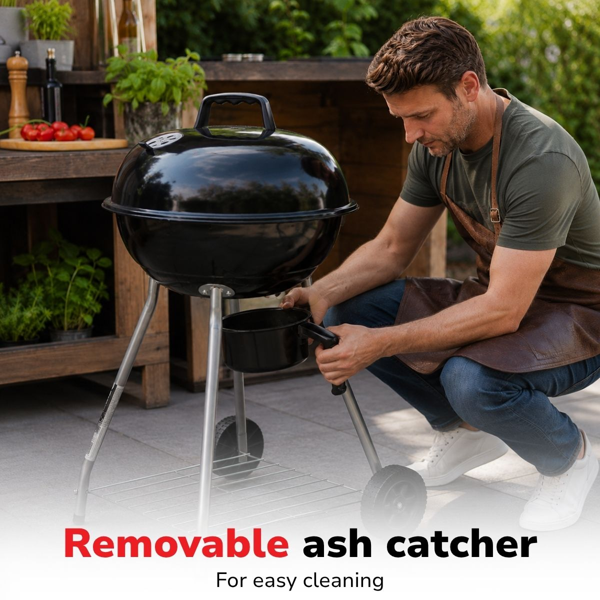A man in a brown apron removes the ash catcher from a black grill.