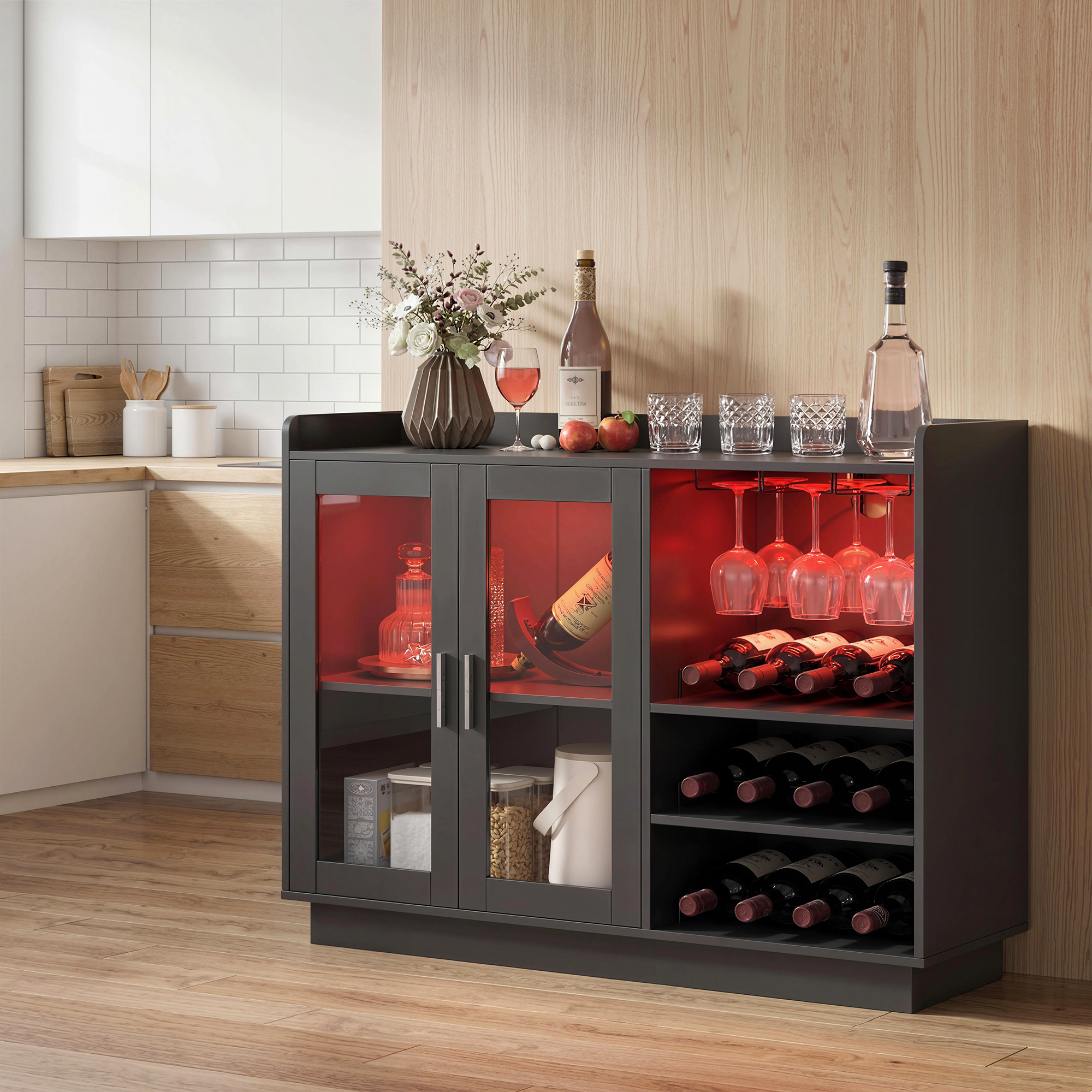 Una credenza scura per vino con bicchieri, bottiglie e luci rosse. Cucina adiacente.