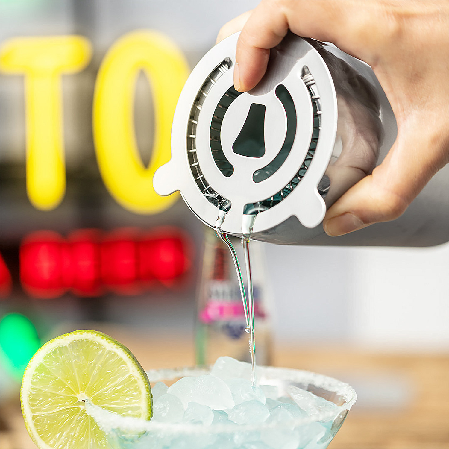 Liquido versato da uno strainer da bar in un bicchiere con ghiaccio e lime.