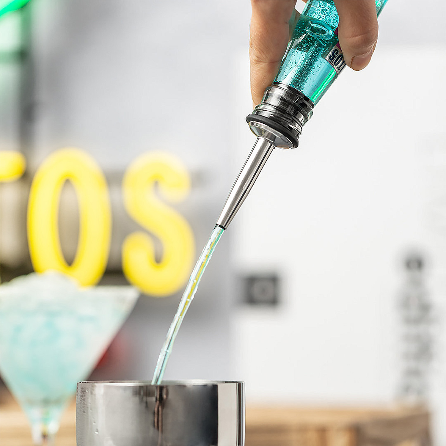 Un liquido blu viene versato da una bottiglia in uno shaker di metallo. Insegna al neon.