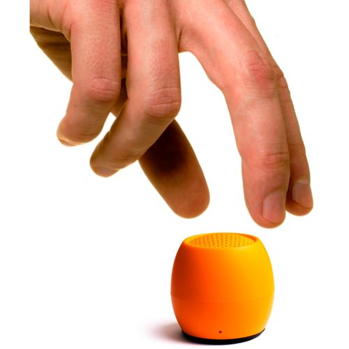 Une main plane au-dessus d'un petit haut-parleur rond orange sur fond blanc.