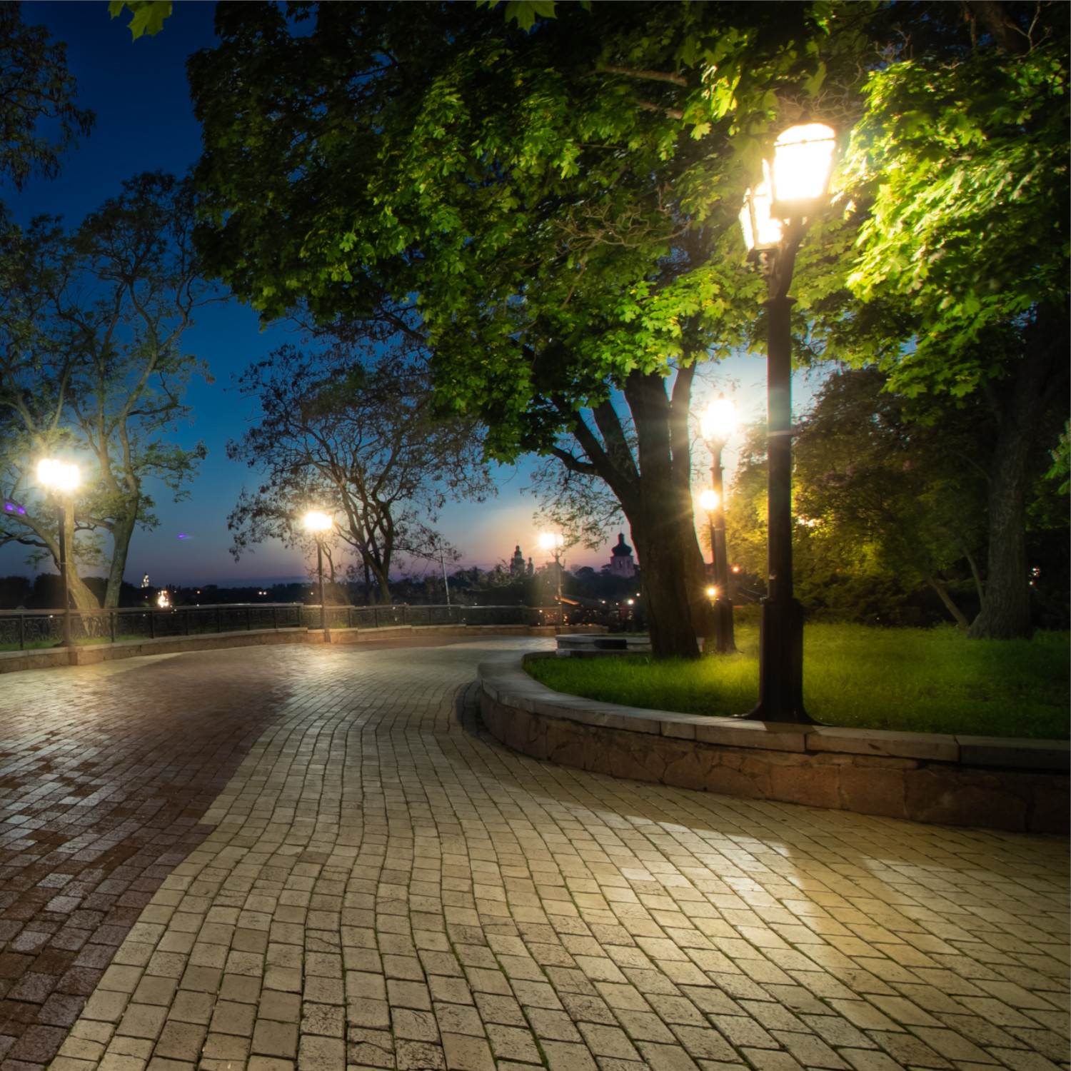 Un sentiero del parco lastricato in pietra illuminato di notte con alberi e lampioni.