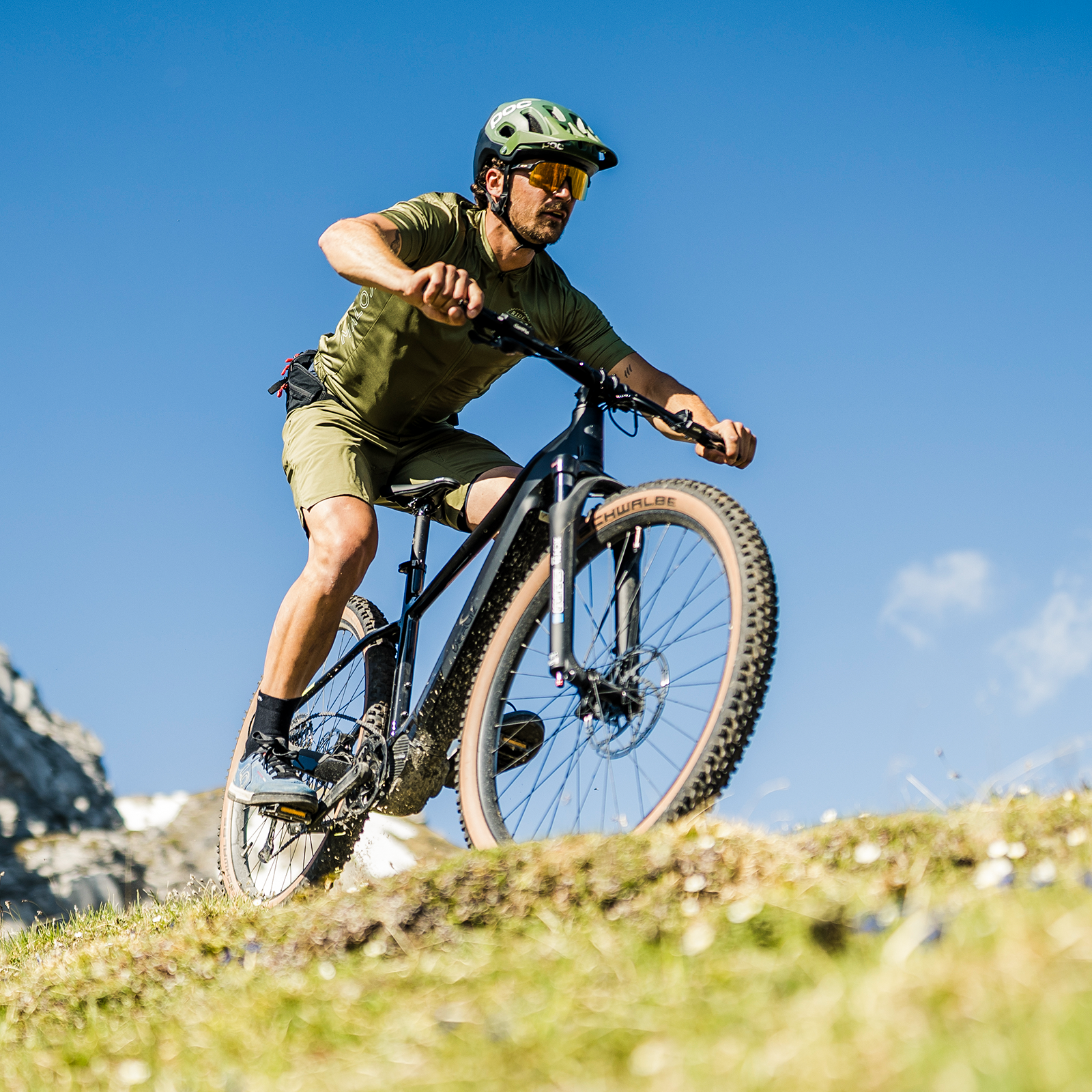 Ein Mann in grüner Kleidung fährt Mountainbike auf einem grasbewachsenen Hang.