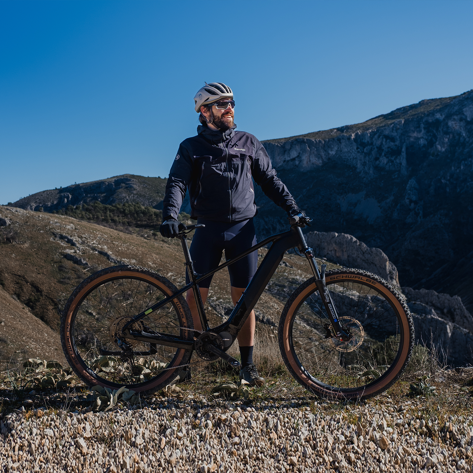 Ein Mann mit Helm und Sonnenbrille steht mit seinem E-Bike auf einem felsigen Hang.