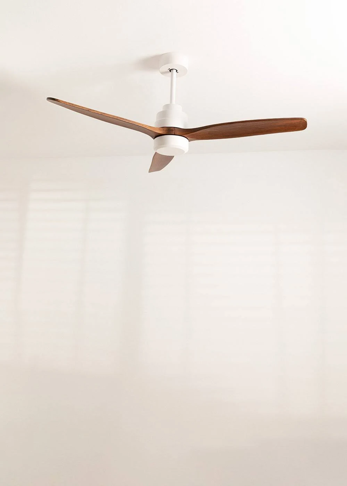 Un ventilador de techo moderno con aspas blancas y de color madera cuelga del techo.