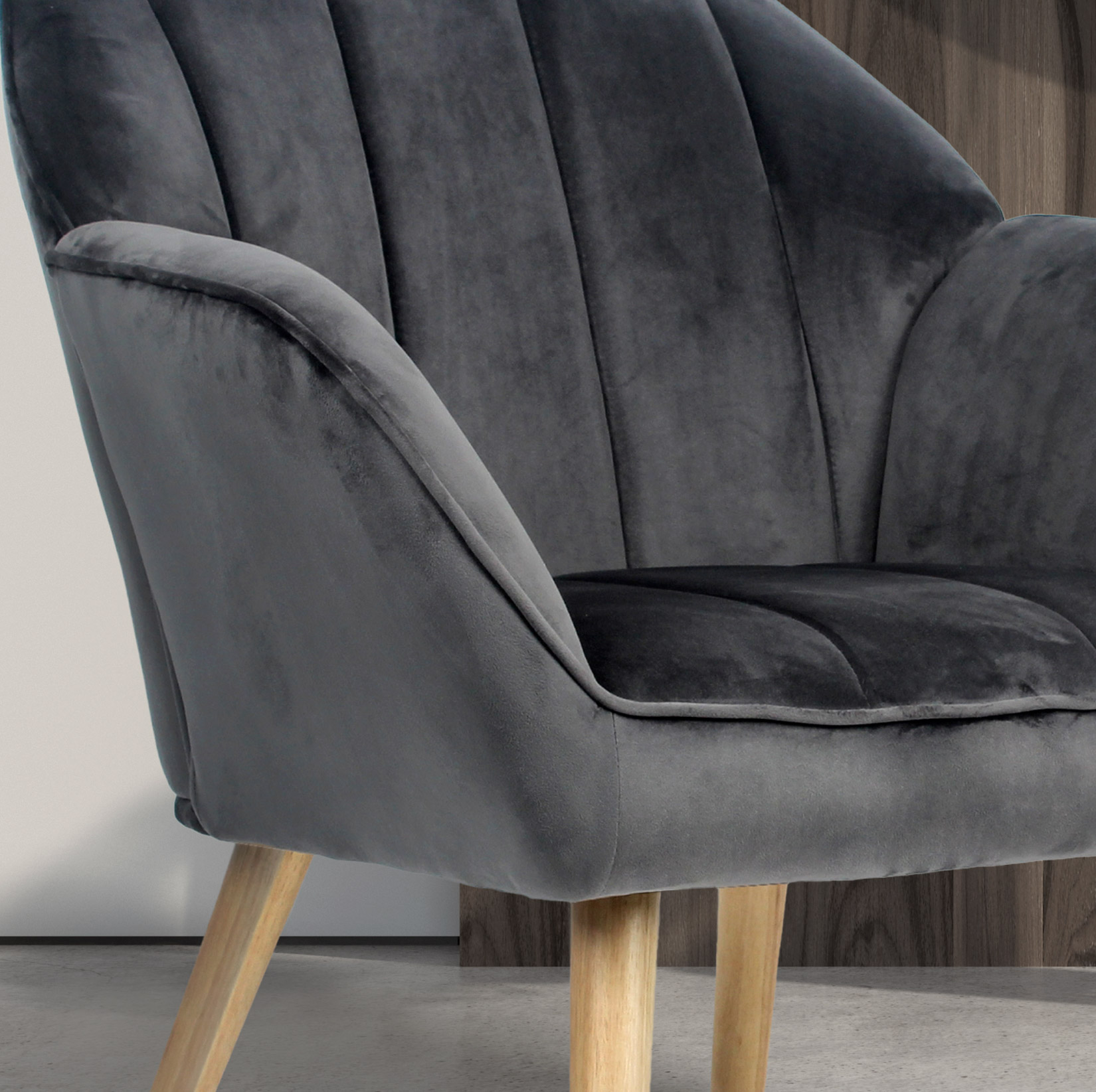 Un sillón tapizado oscuro con patas de madera se asienta sobre un suelo de hormigón.