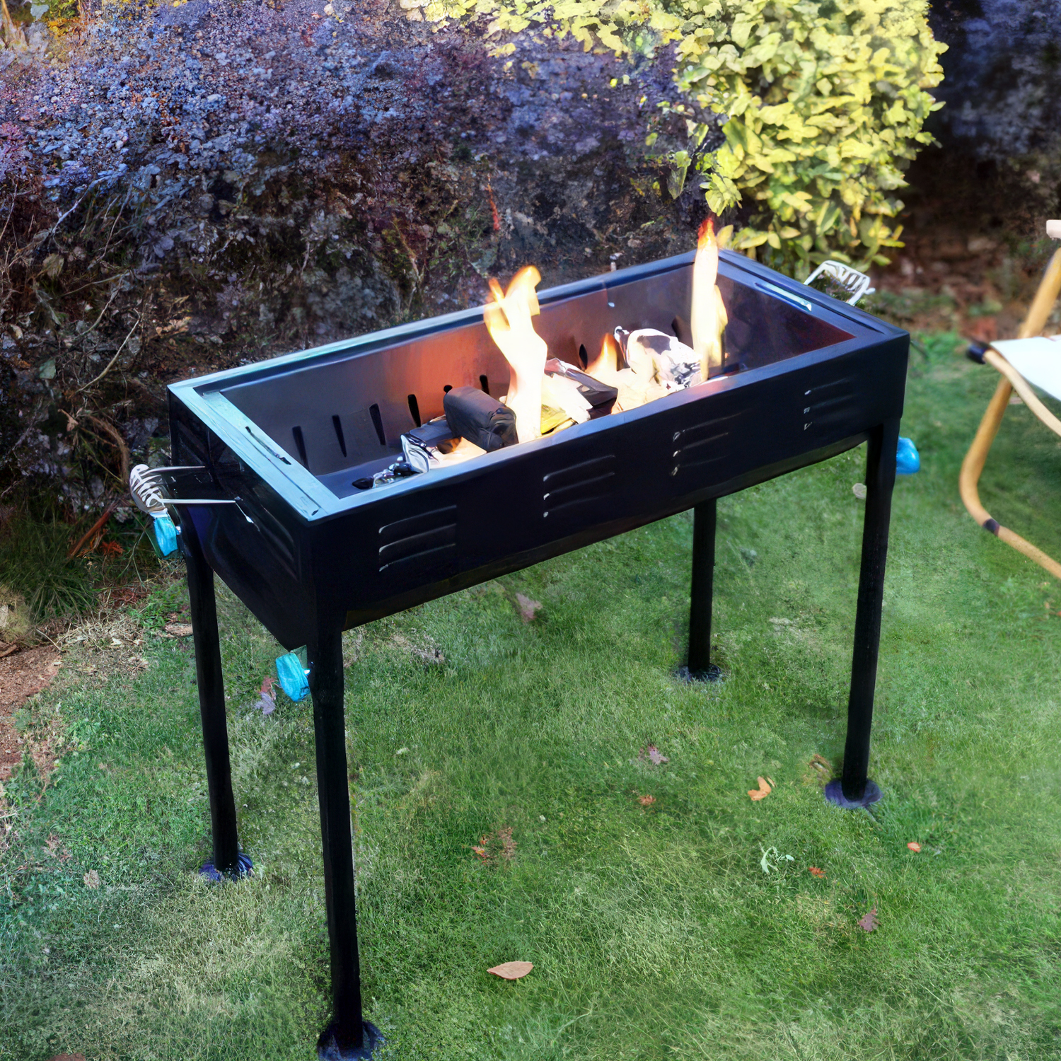 Ein schwarzer Grill mit Flammen auf einem grünen Rasen, im Hintergrund Büsche.
