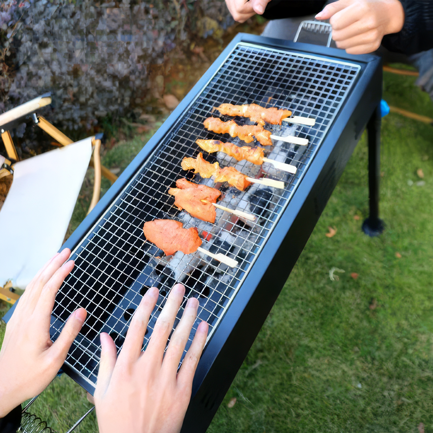 Hände wärmen sich an einem Grill mit Fleischspießen auf einem Rost über glühender Kohle.