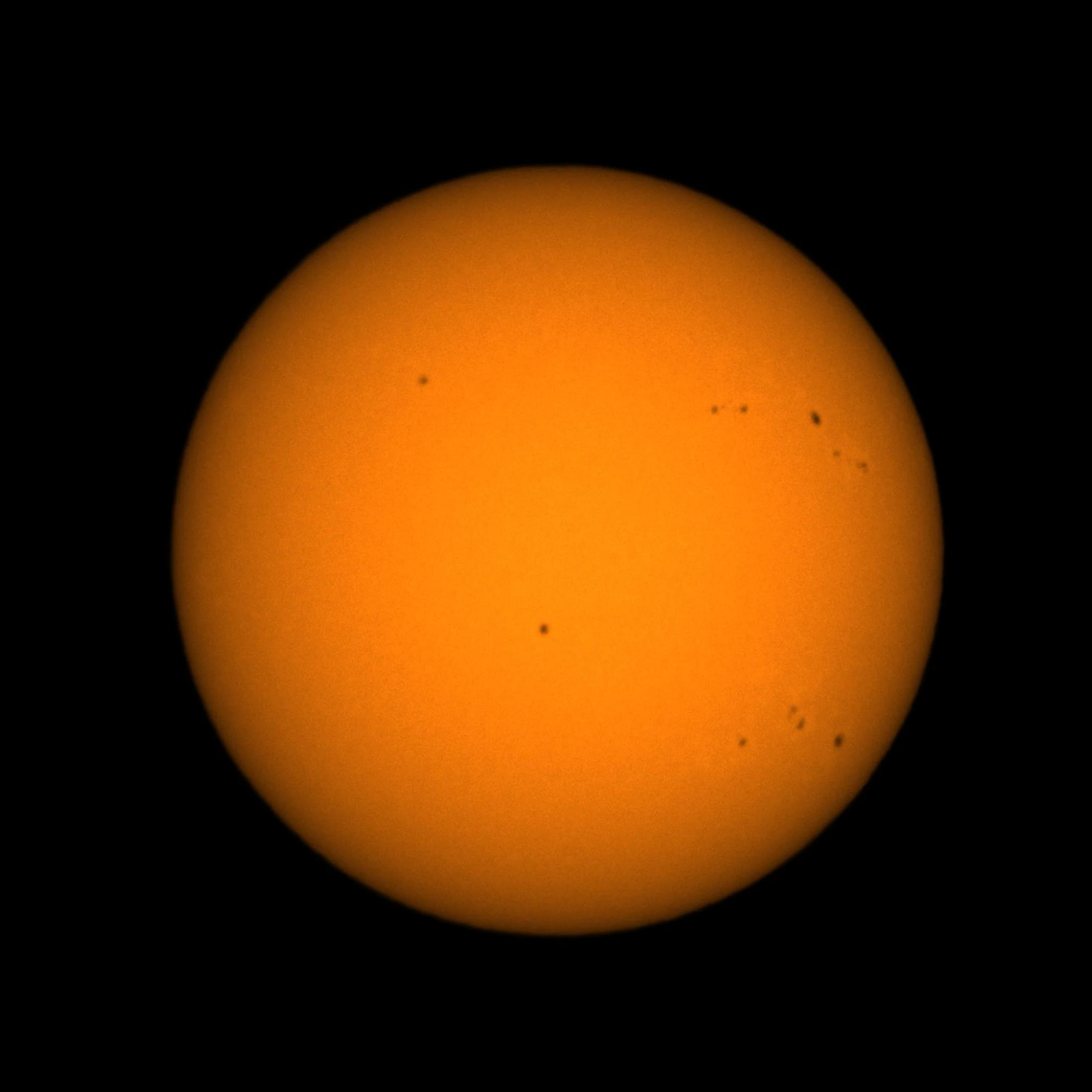 Die Sonne mit sichtbaren Sonnenflecken vor schwarzem Hintergrund.