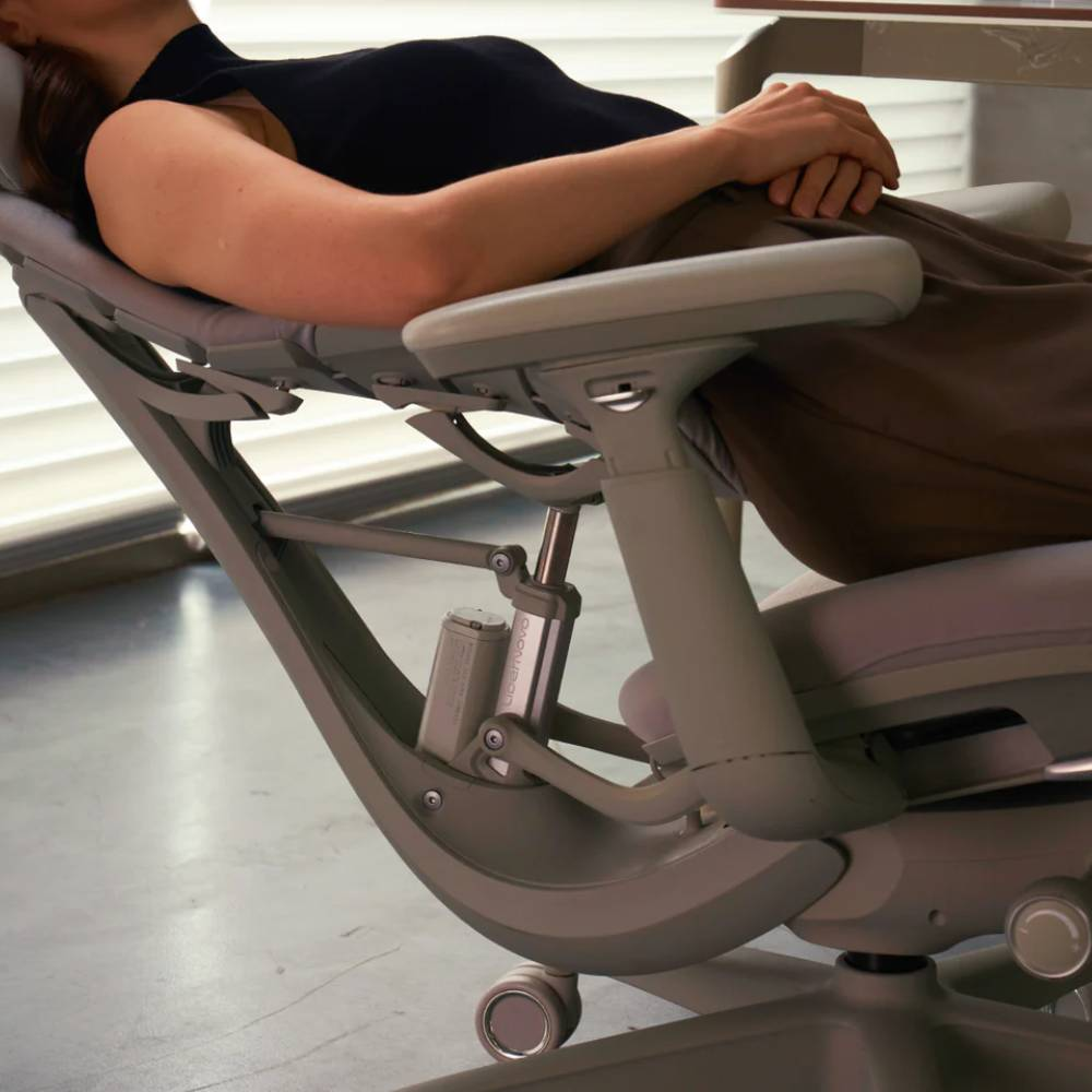 Une personne en haut noir et pantalon marron s'allonge dans un fauteuil de bureau gris.