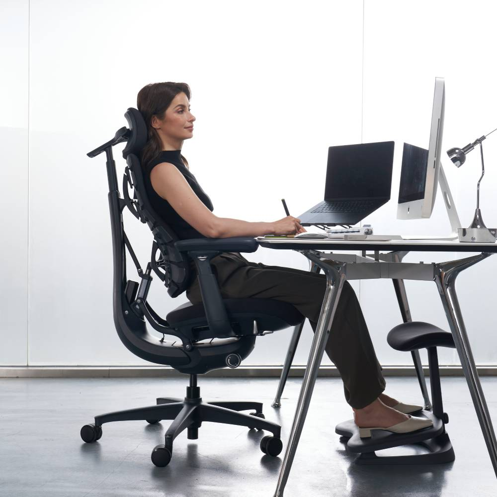 Eine Frau sitzt an einem Schreibtisch und benutzt einen Laptop und einen Computer.