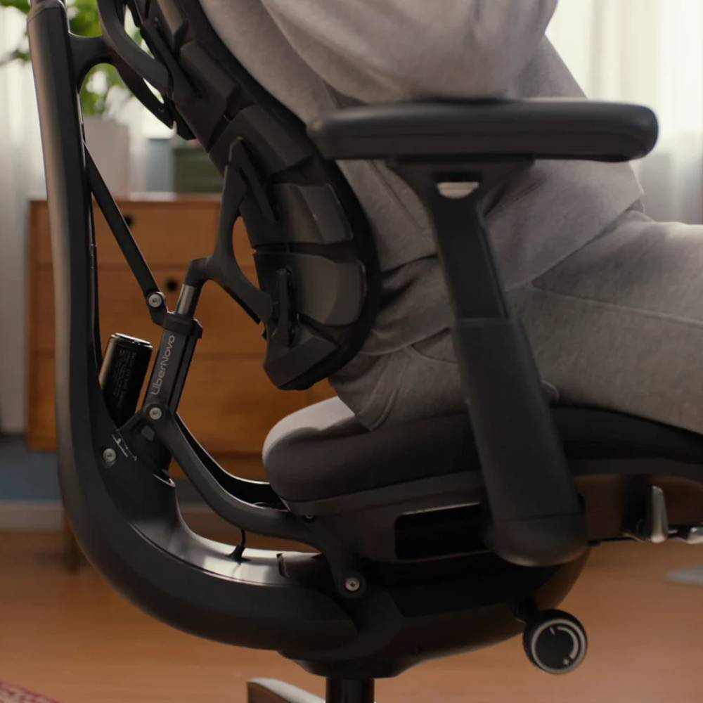 Personne assise dans un fauteuil de bureau noir avec dossier et accoudoirs réglables.