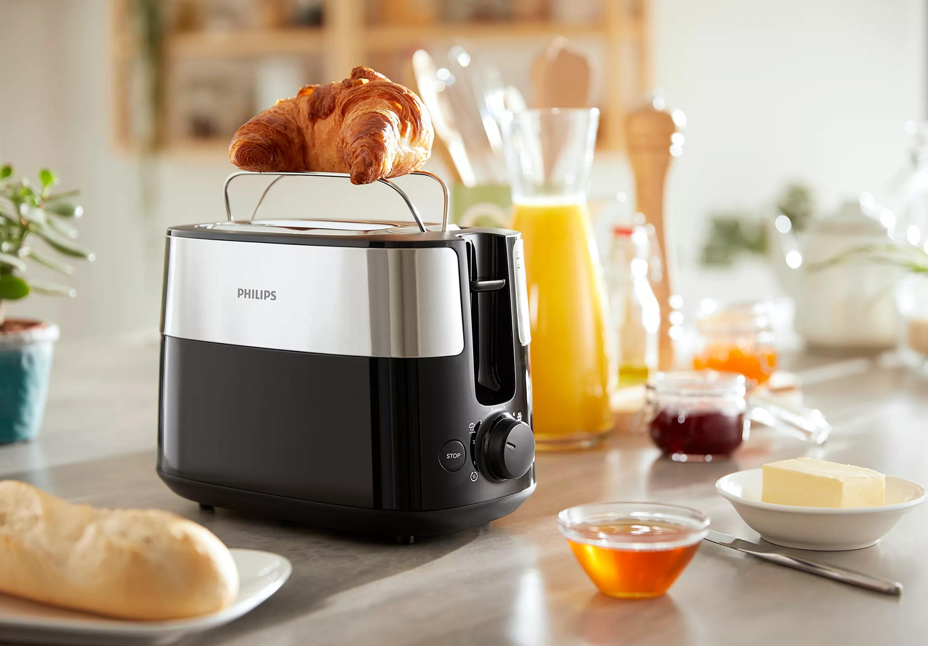 Ein schwarzer Toaster mit einem Croissant, daneben Honig, Marmelade und Butter.